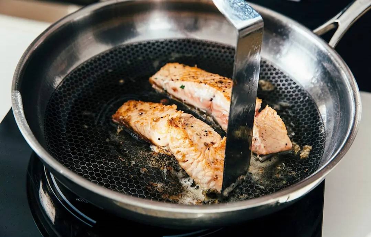 Lasta kääntämässä lohifileitä hunajakennokuvioisessa Heirol Steelsafe paistinpannussa.