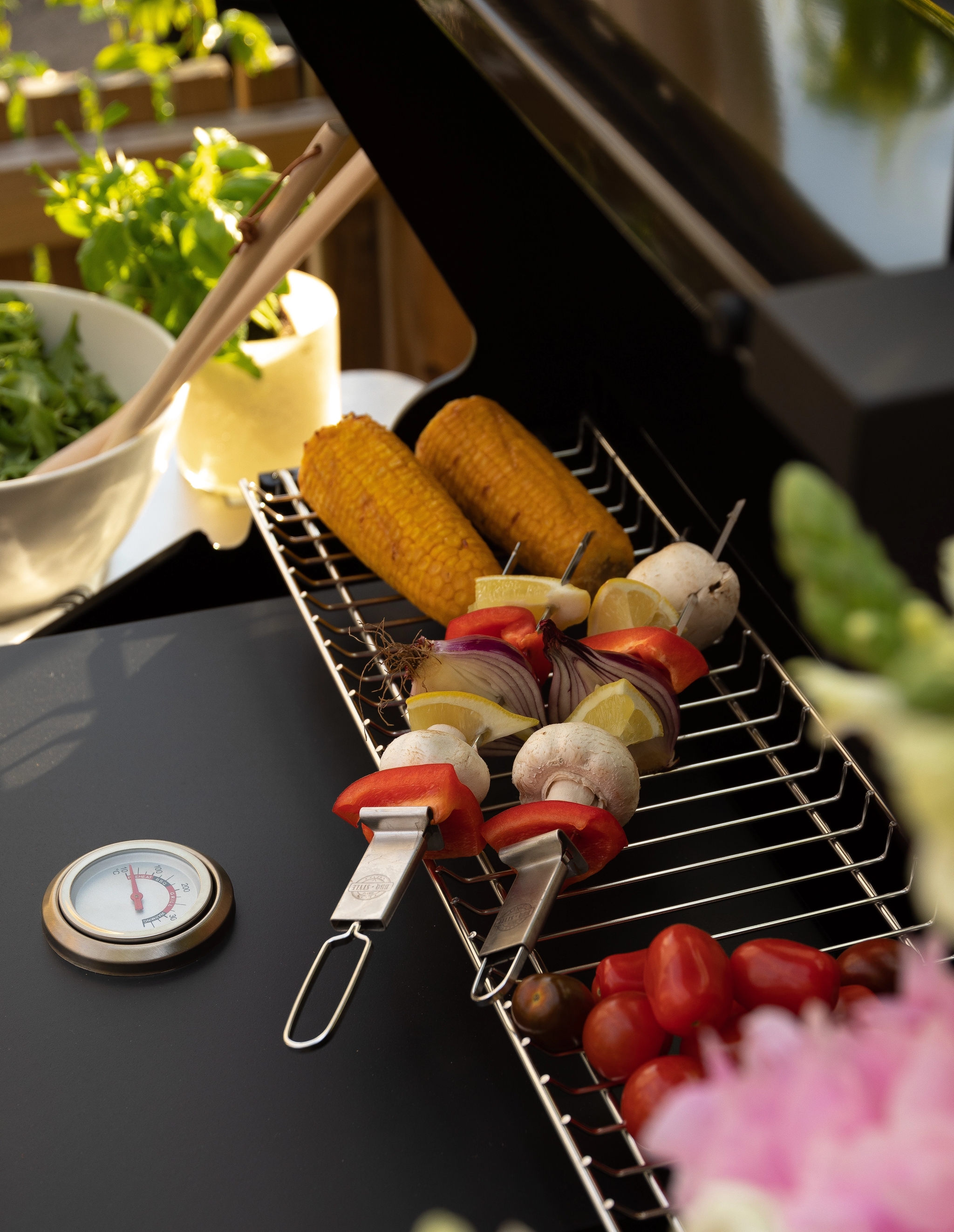Majs, grönsaksspett och tomater på ett grillgaller bredvid en termometer