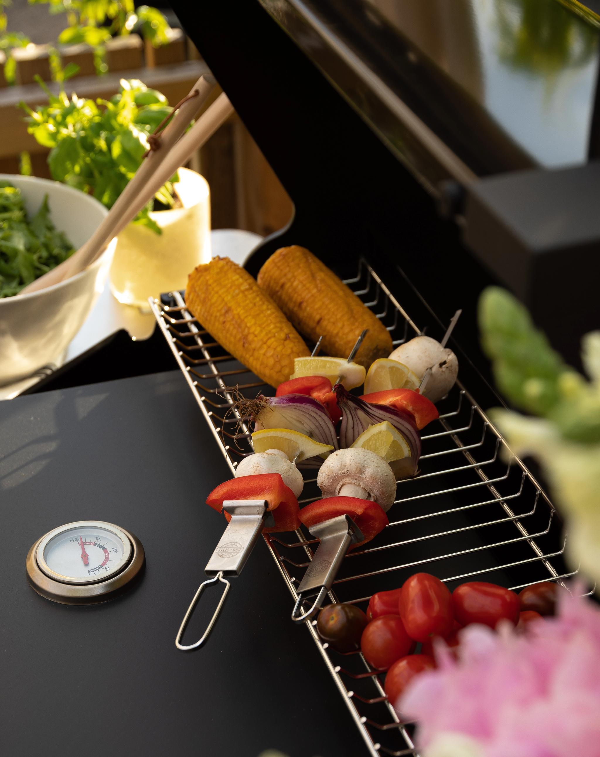 Majs, grönsaksspett och tomater på ett grillgaller bredvid en termometer