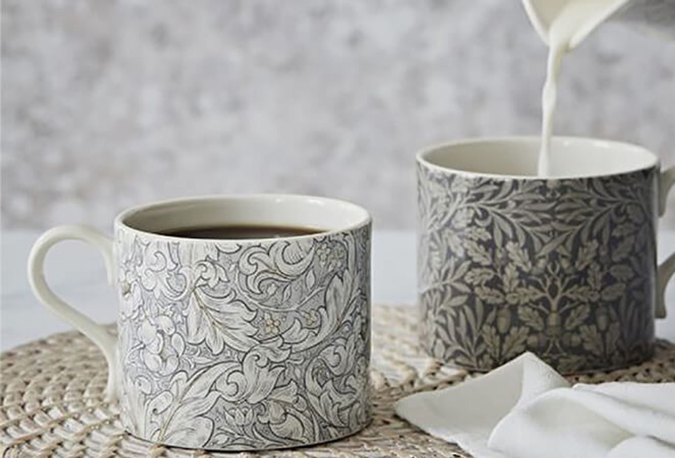 Två William Morris muggar med blommönster, stående på ett bordsunderlägg