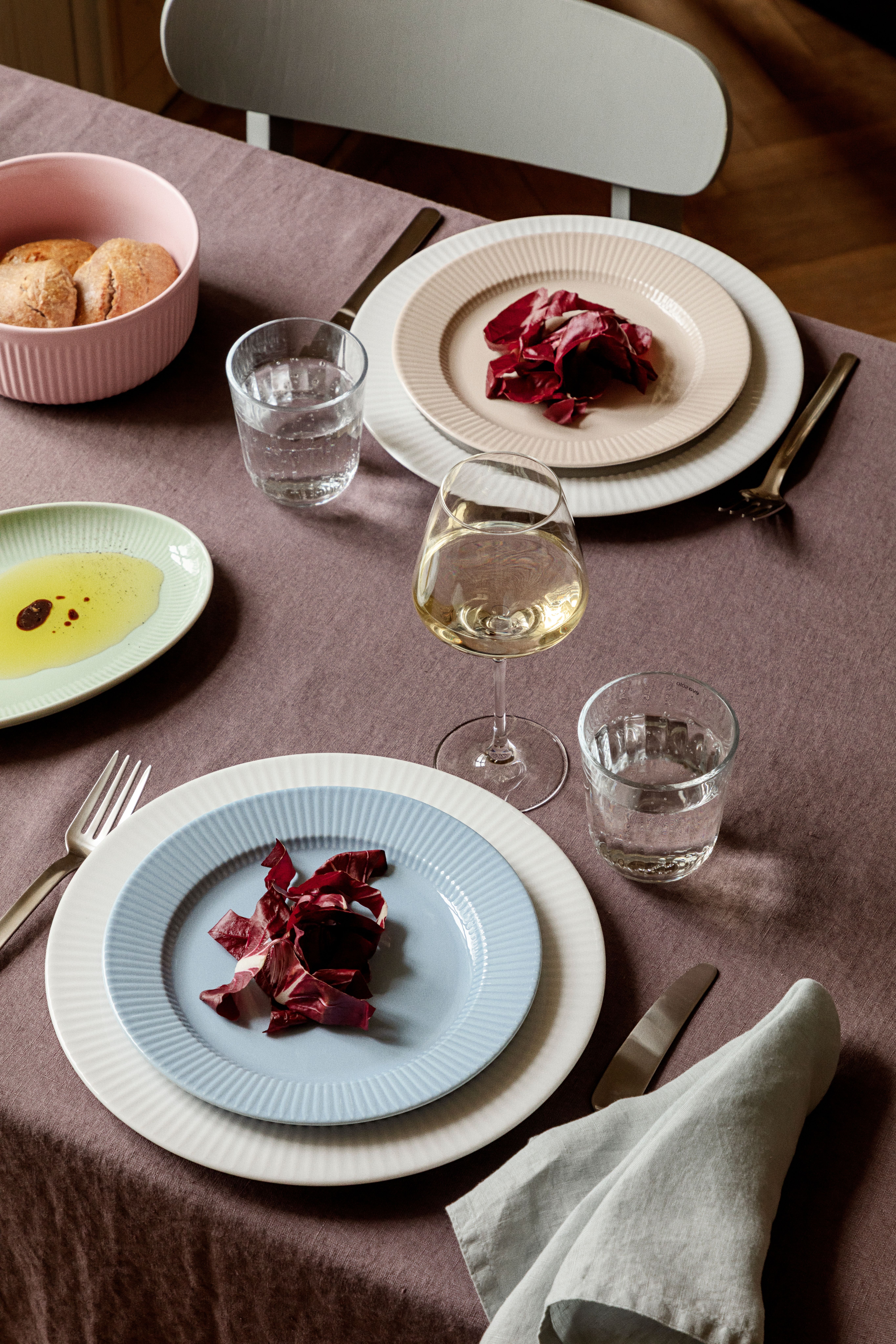Dukat matbord med räfflade tallrikar, radicchiosallad, bröd samt glas med vatten och vitt vin.