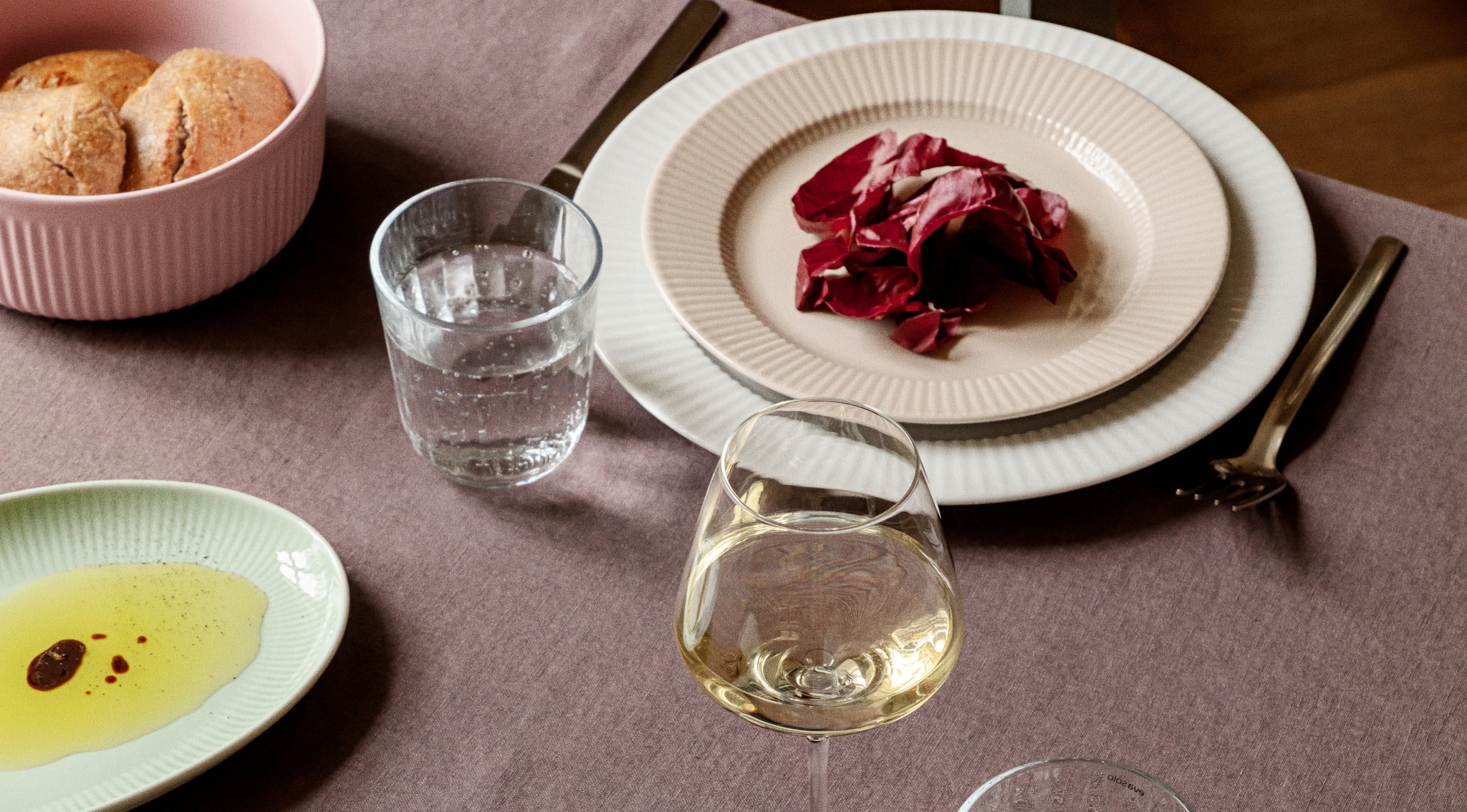 Dukat matbord med räfflade tallrikar, radicchiosallad, bröd samt glas med vatten och vitt vin.