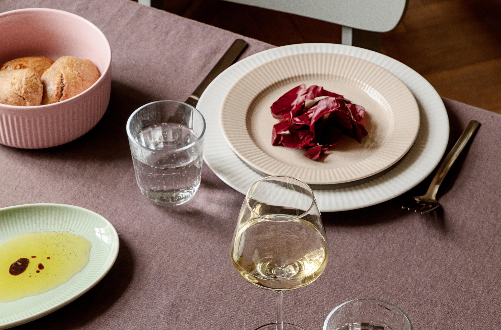 Elegant dukning med räfflat porslin, radicchiosallad, bröd samt glas med vatten och vitt vin.