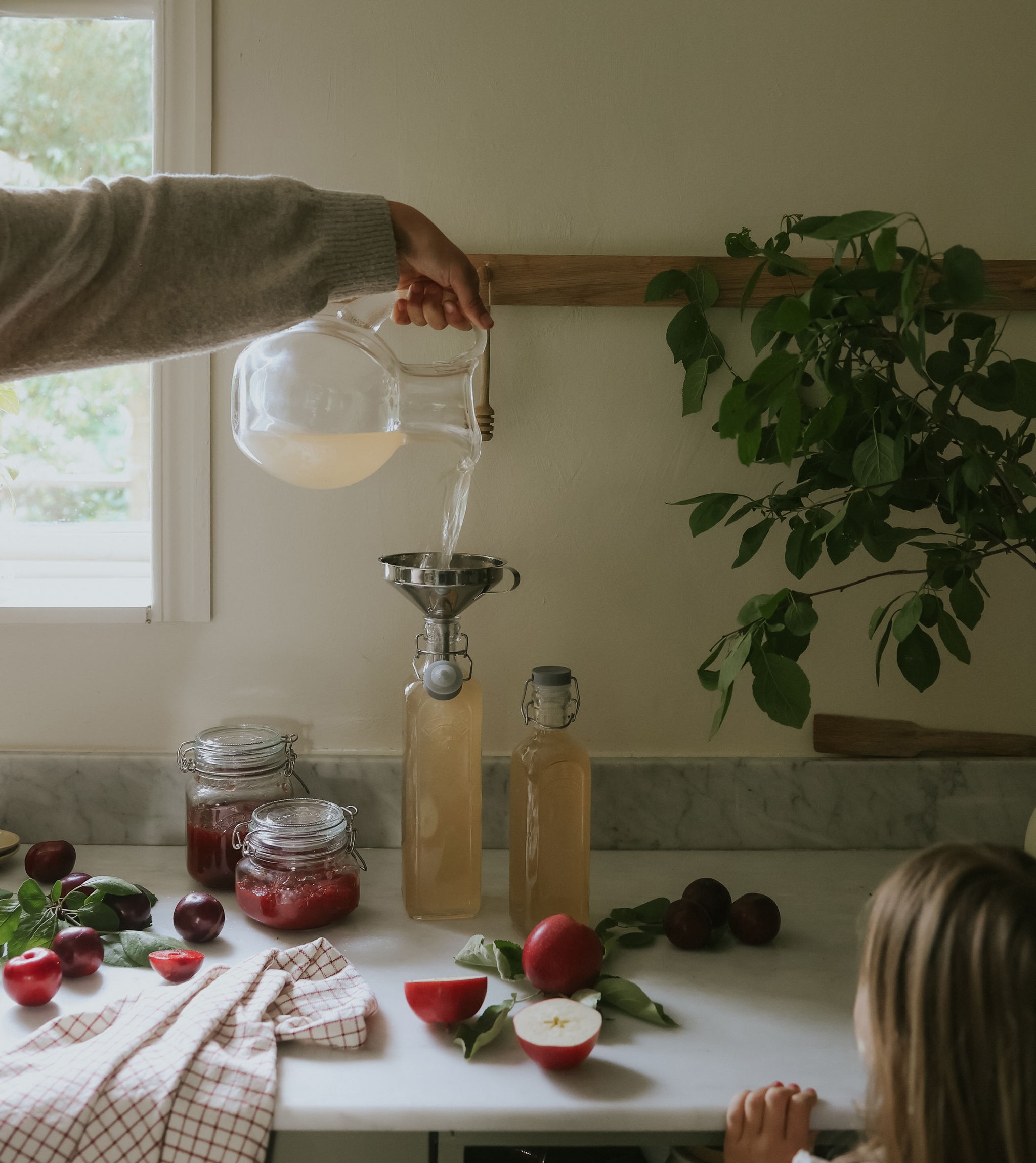 En person som häller upp nykokt hemmagjord saft på flaskor i ett lantligt kök