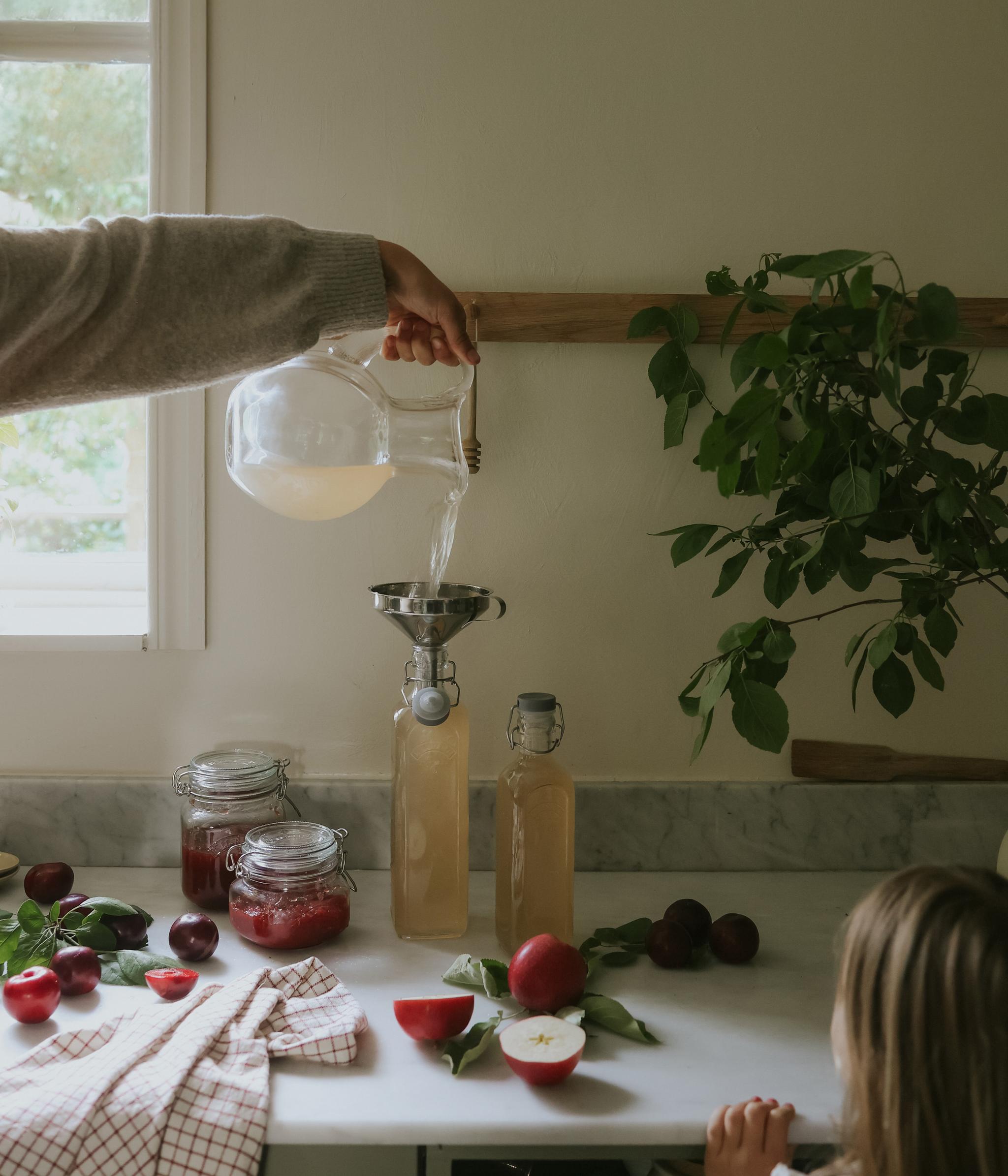 En person som häller upp nykokt hemmagjord saft på flaskor i ett lantligt kök