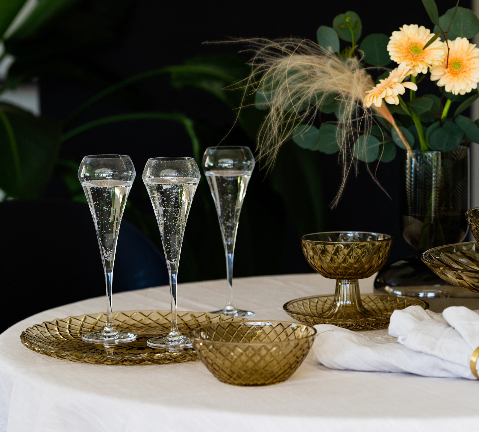 Ett dukat bord med champagneglas, glasskålar och en vas med gula blommor