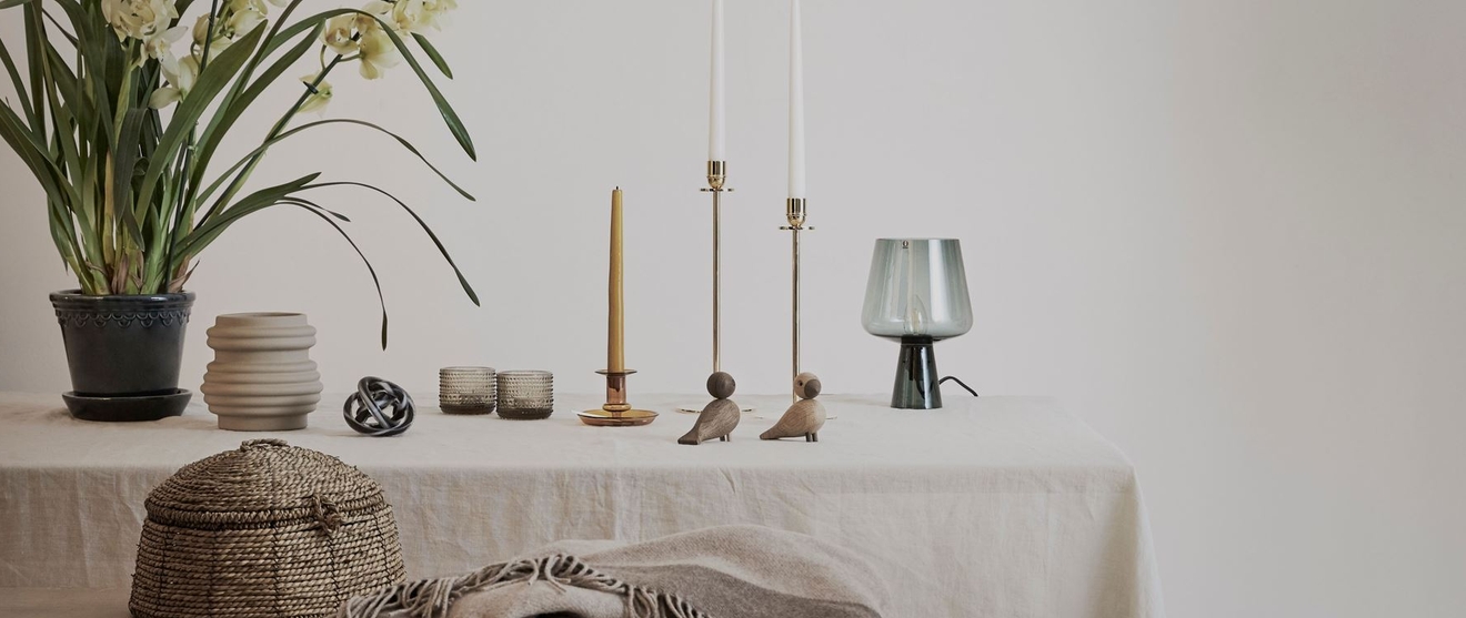 Innredning, lysestaker, lyslykter, vaser og ligende på bord med beige linduk