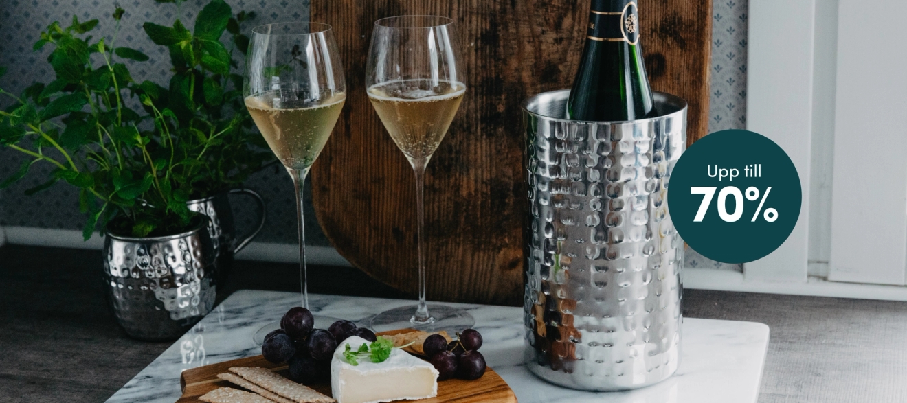  Två champagneglas, en flaska i en hamrad vinkylare, ost, kex och vindruvor på en marmoryta