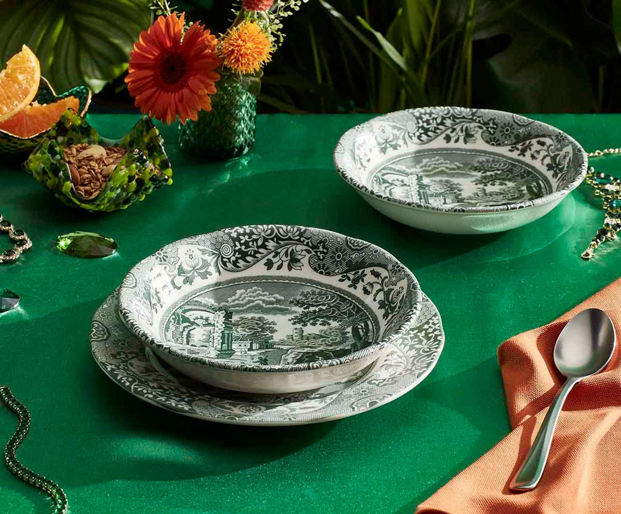 Elegant borddekking med svart-hvitt mønstret servise, blomster og appelsin på en grønn duk.