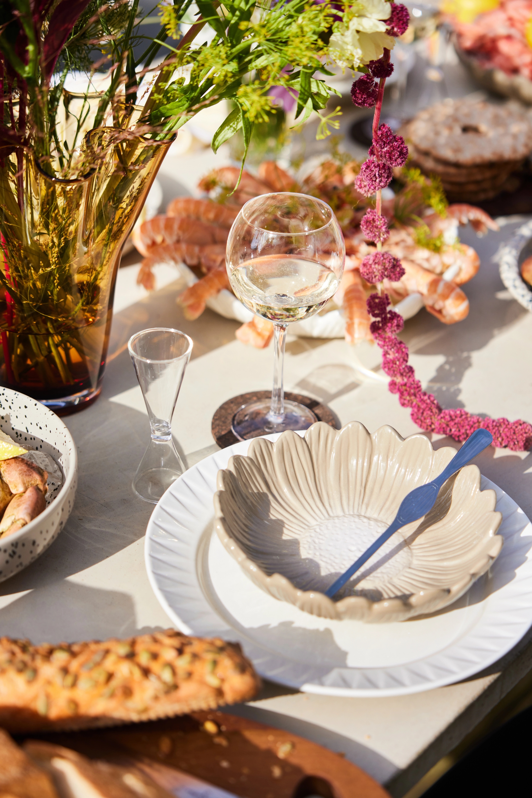 Äyriäisbuffet Pöydänkattaus jossa lauset kulhot snapsilatis ja viinilasit ruoan ja kukkien kera