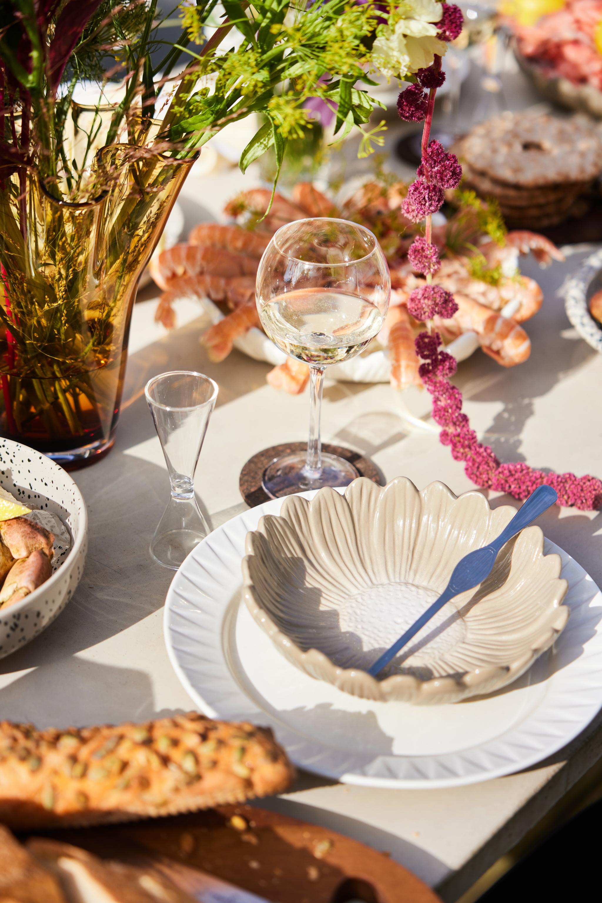 Äyriäisbuffet Pöydänkattaus jossa lauset kulhot snapsilatis ja viinilasit ruoan ja kukkien kera