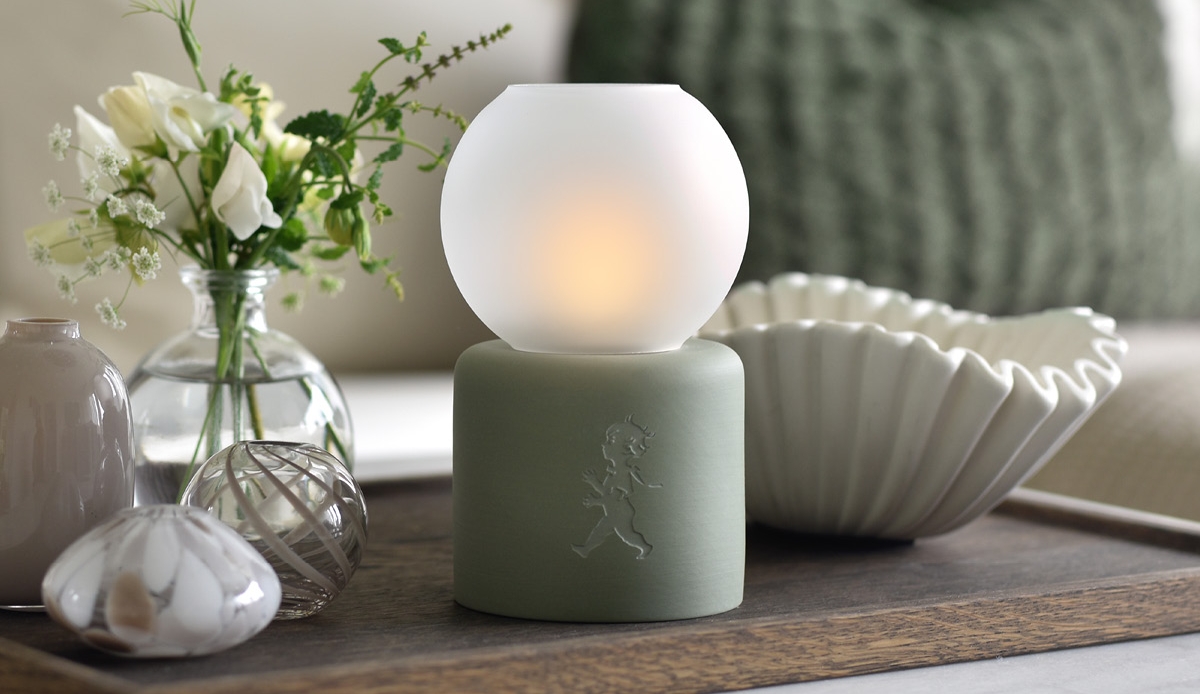 Stämningsfull bordslampa med frostat glas och grön fot bland blommor och dekorativa föremål.