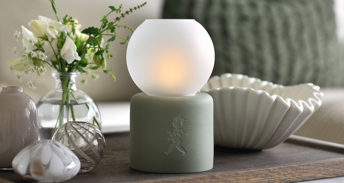 Stemningsfull borddekorasjon med lysende lampe, hvite blomster og keramikk på et trefat.