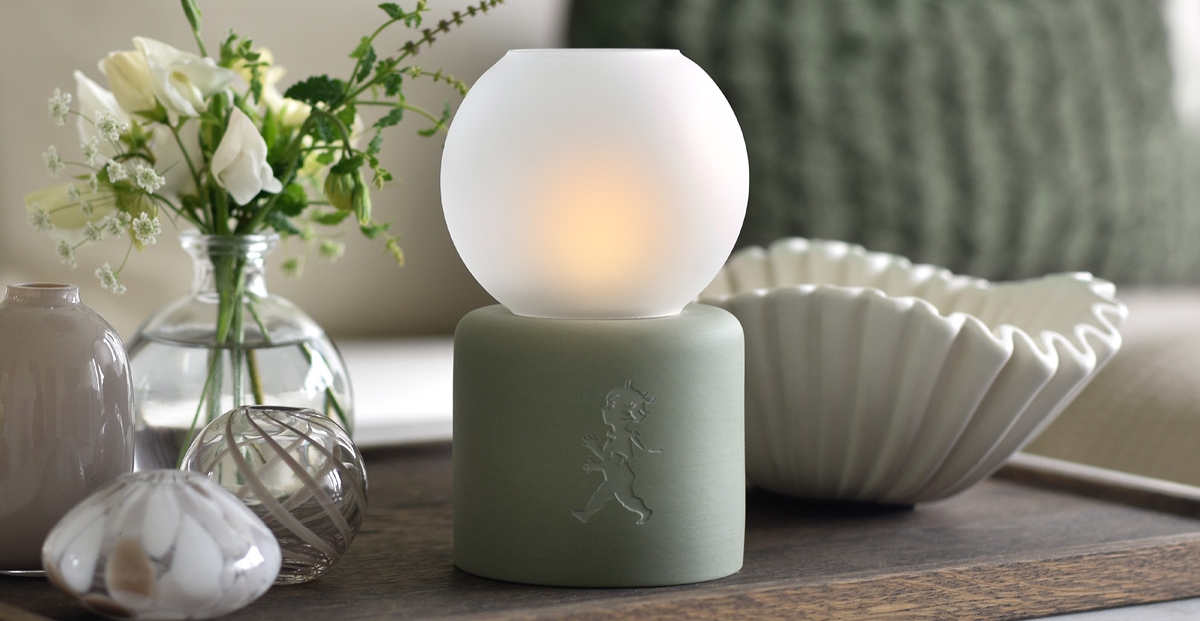 Stemningsfull bordlampe med frostet glasskuppel, omgitt av hvite blomster og dekorative vaser på et trebord.