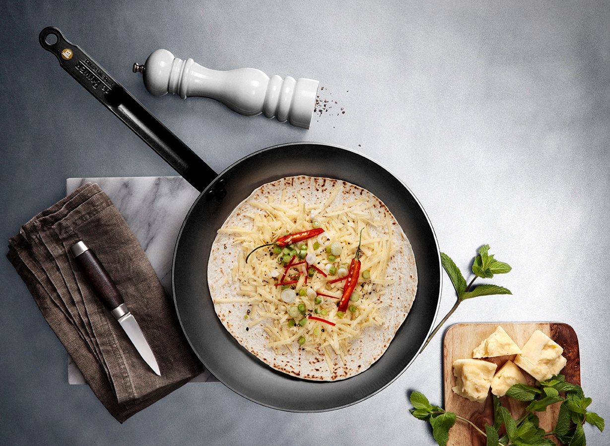 Paistinpannulla paistuva tortilla on täytetty juustoraasteella, chilillä ja kevätsipulilla tyylikkäässä keittiöasetelmassa.