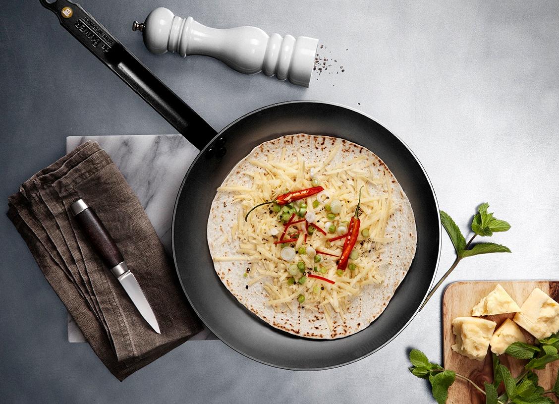 Paistinpannulla paistuva tortilla on täytetty juustoraasteella, chilillä ja kevätsipulilla tyylikkäässä keittiöasetelmassa.