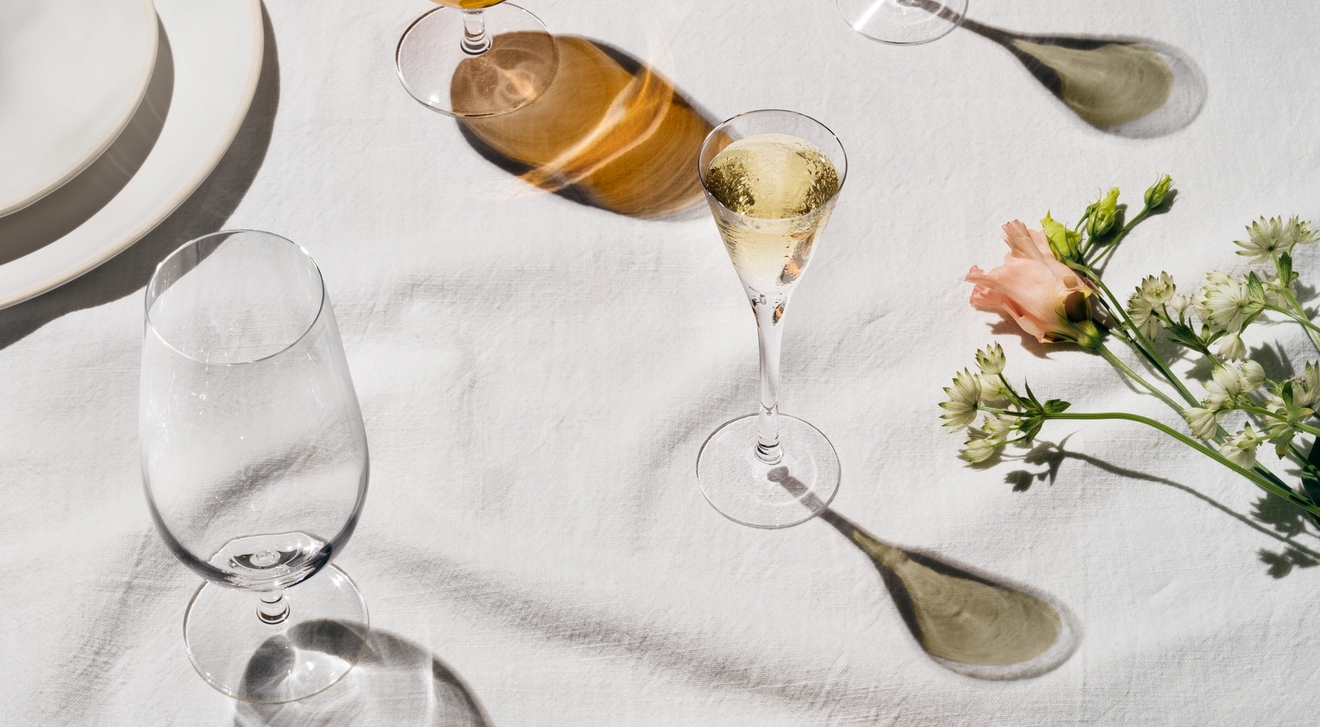 Lyst og elegant dekket bord med øl, musserende vin, poteter og vårgrønnsaker på hvit duk.