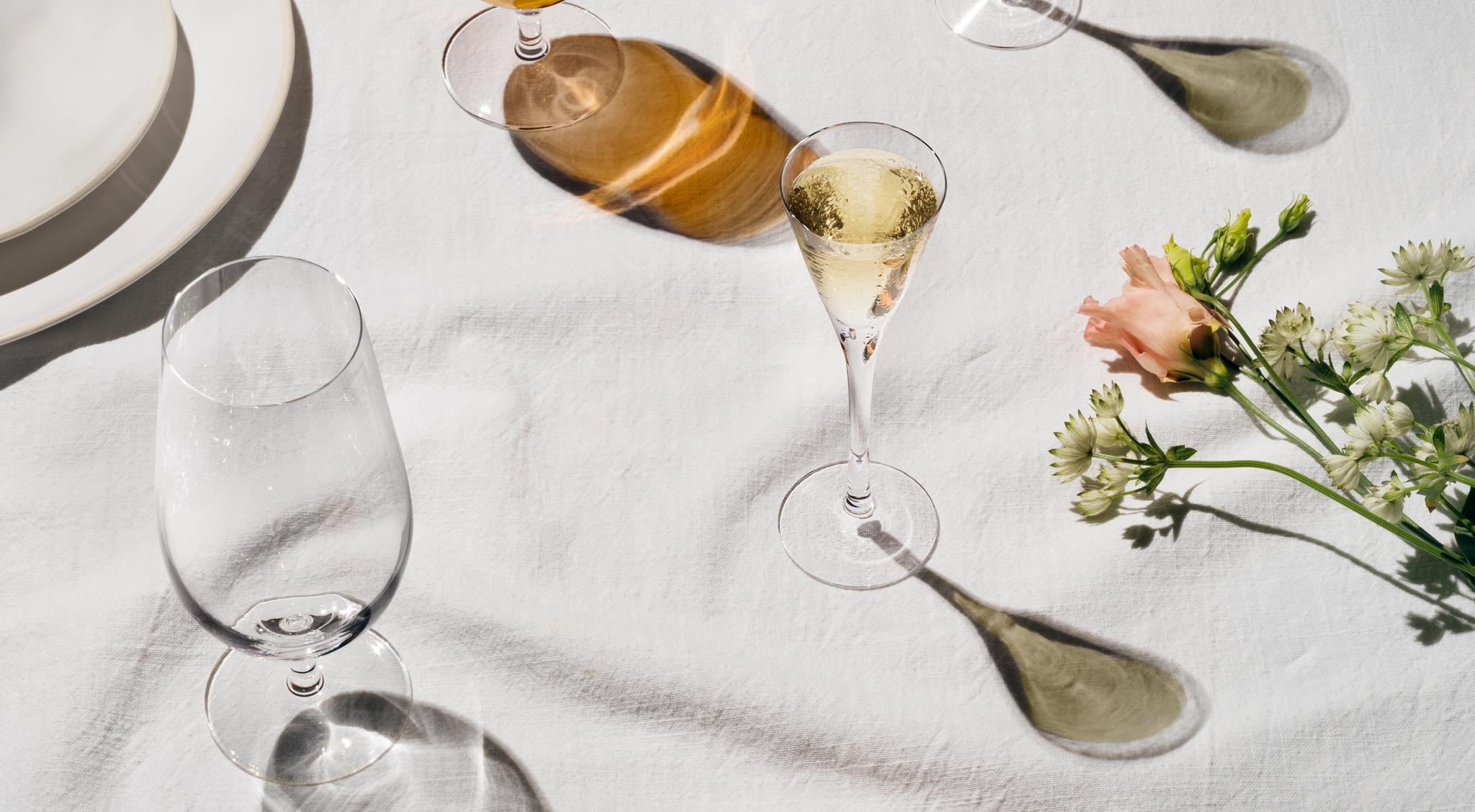 Lyst og elegant dekket bord med øl, musserende vin, poteter og vårgrønnsaker på hvit duk.