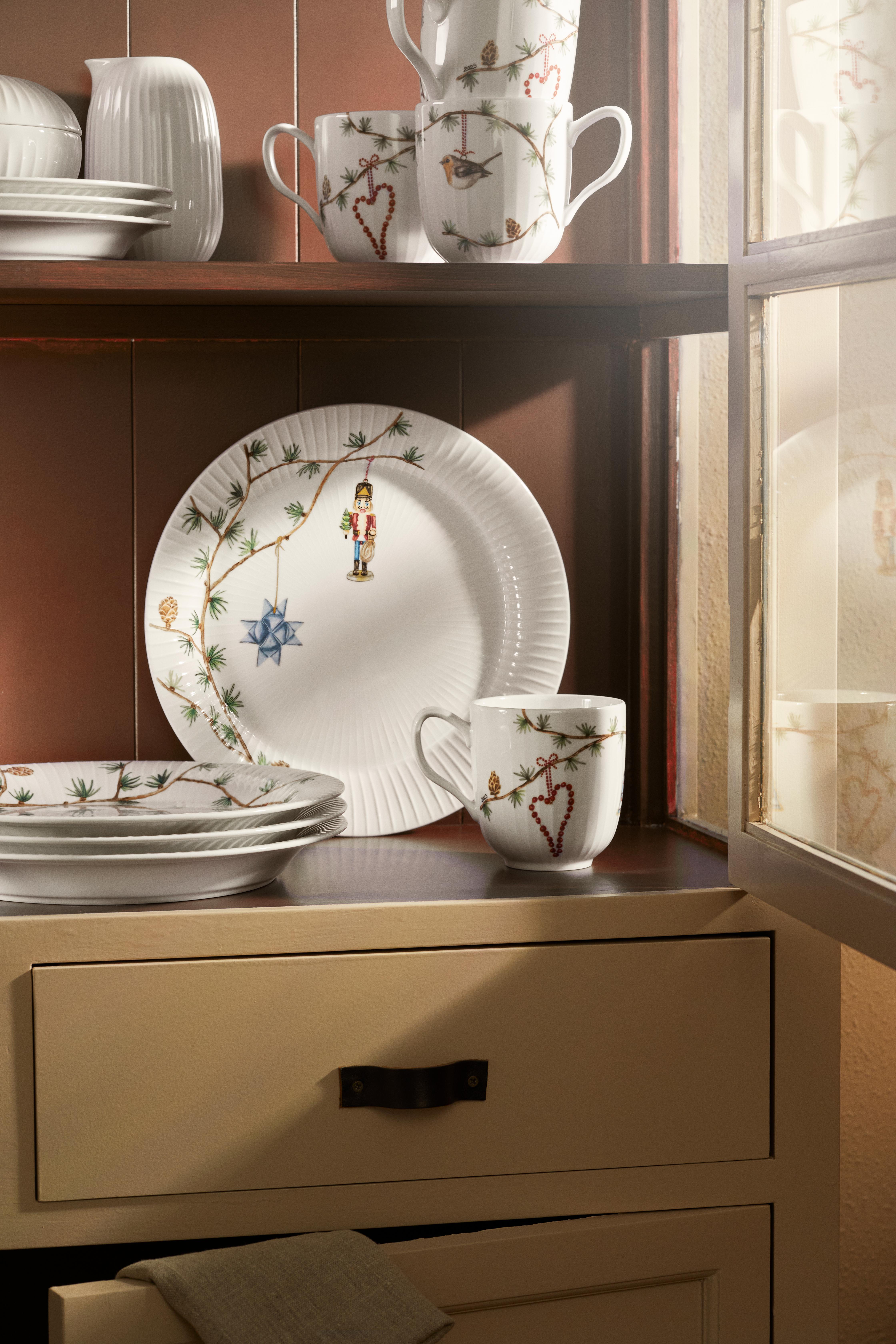 Hvitt juletema-servise med nøtteknekker-, fugle- og furuguver-design utstilt i et treskap.