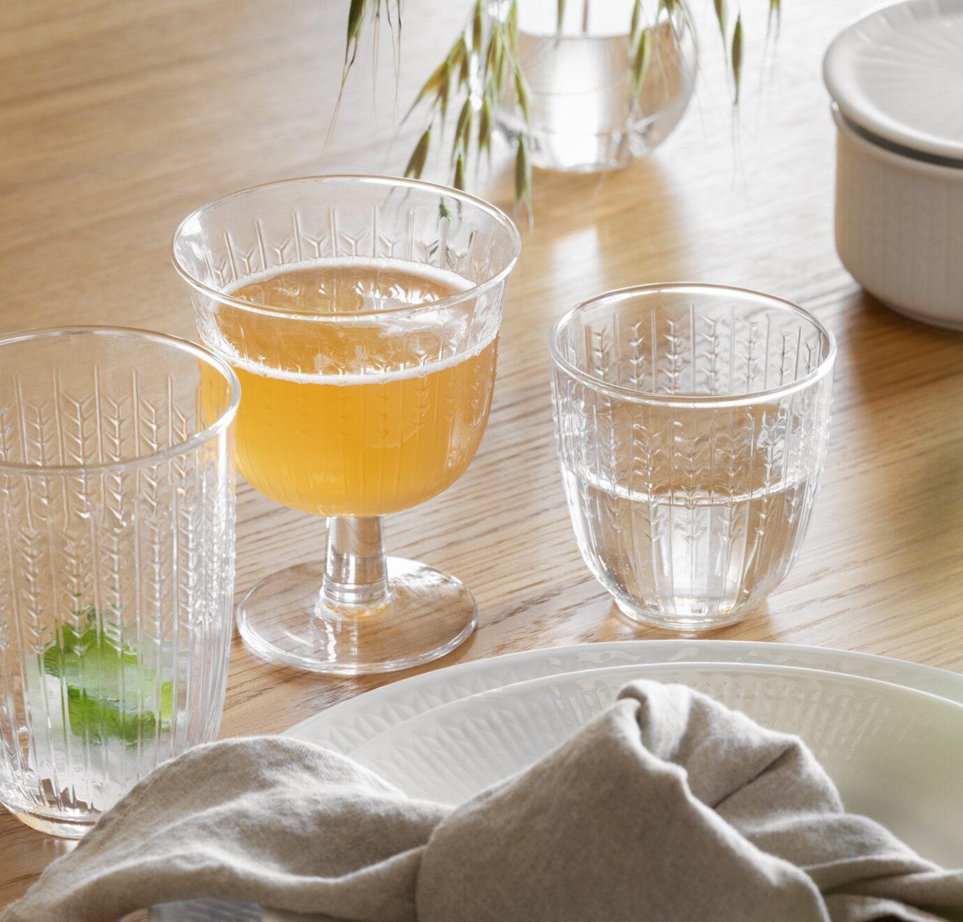 Elegant borddekking med hvitt servise, linserviett og mønstrede glass på et lyst trebord.