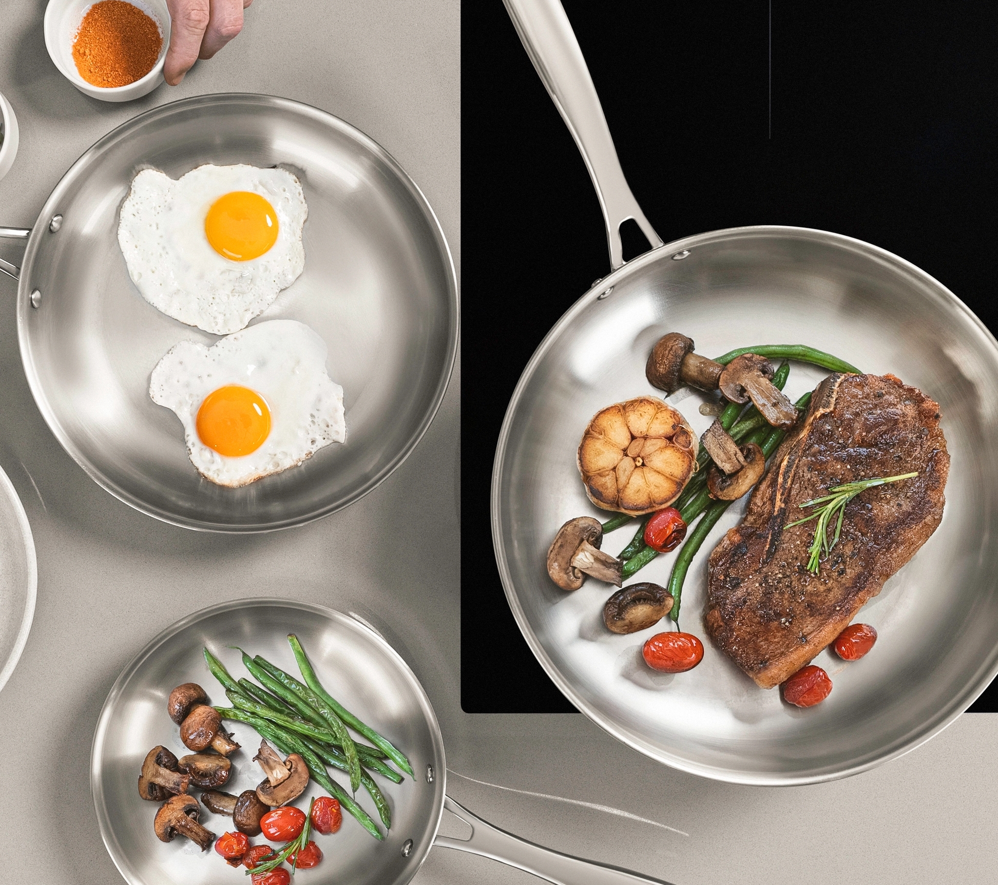 Matlagning i rostfria stekpannor med stekt ägg, kött, svamp, sparris och tomater på en induktionshäll.
