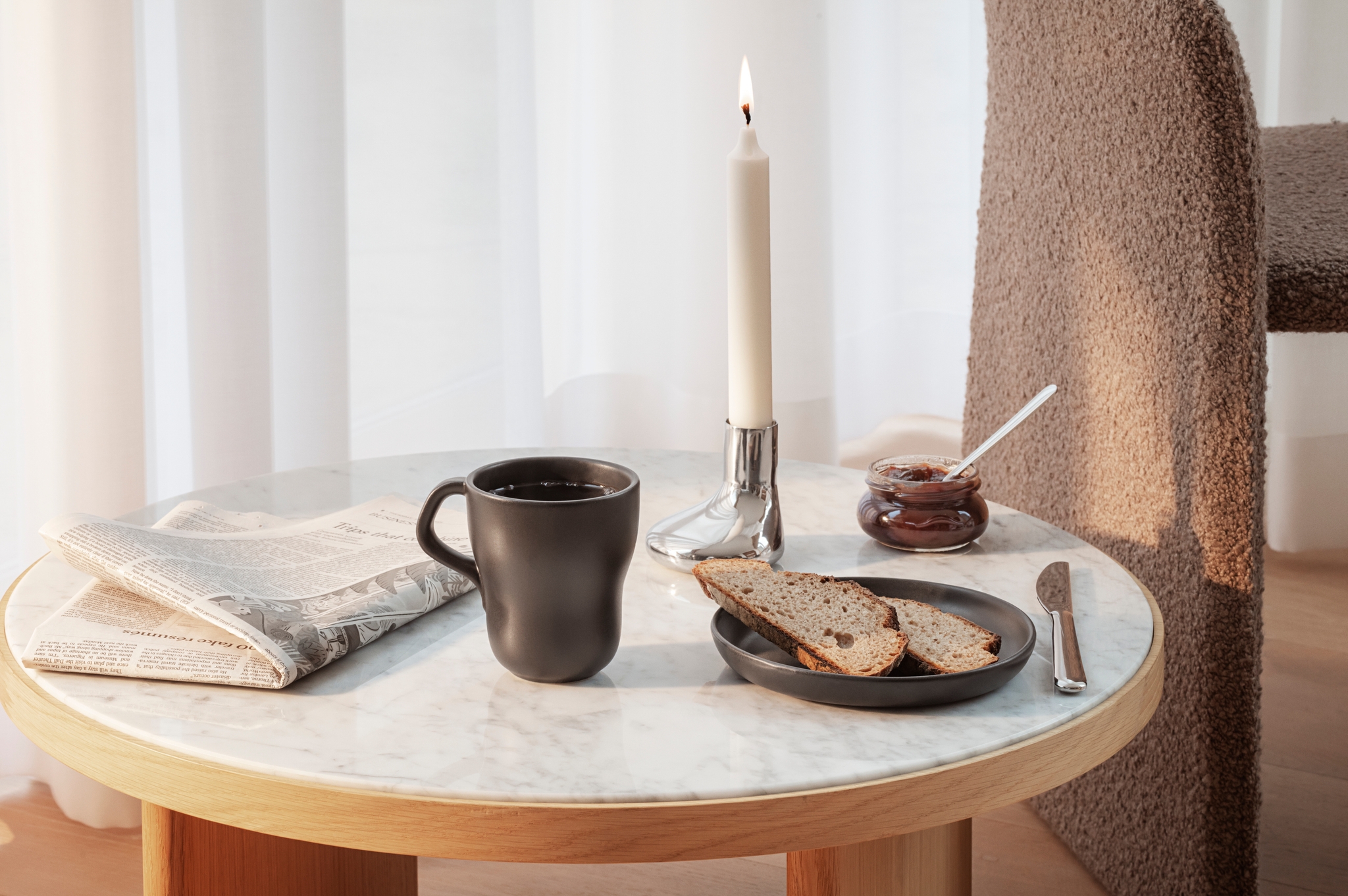 Ljusstake från eva solo står tänt på ett bord tillsammans med en kaffemugg, samt en tidning