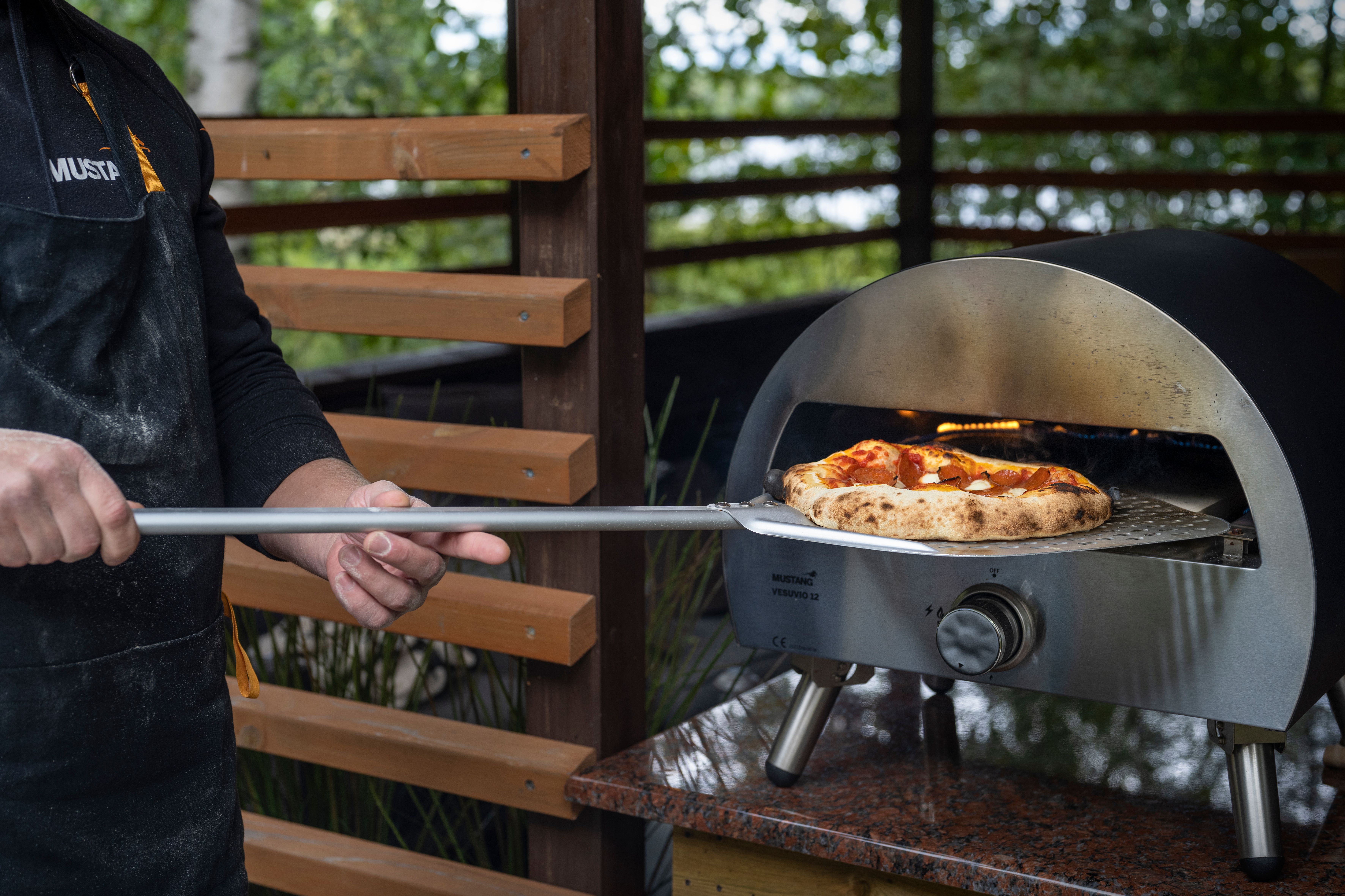 En svart kolgrill från Broil King står på en träaltan med gröna träd i bakgrunden