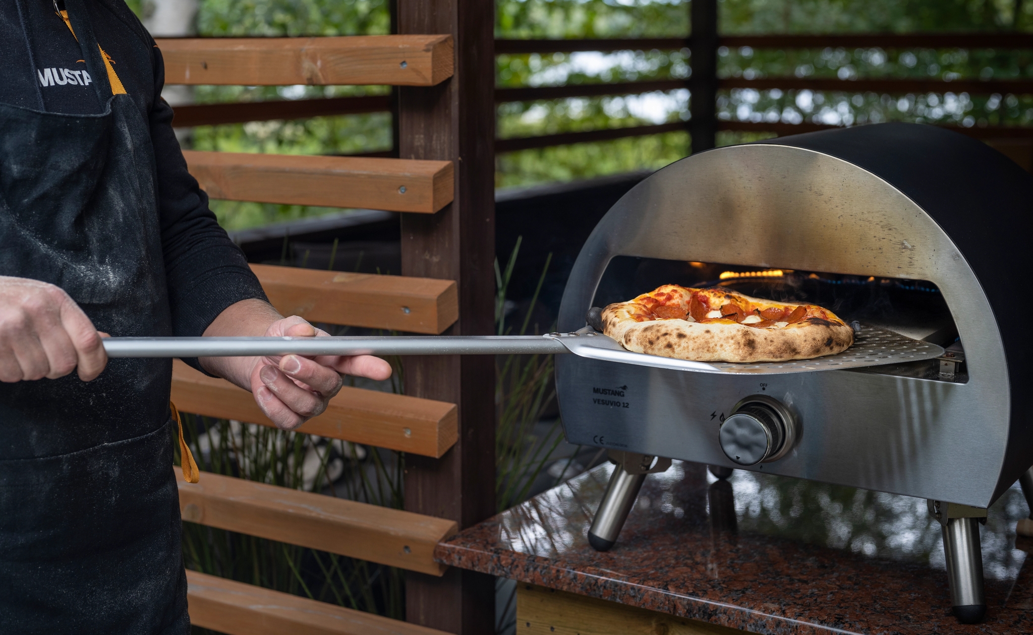 En man skjuter in en pizza med en pizzaspade i en utomhus gasdriven pizzaugn.