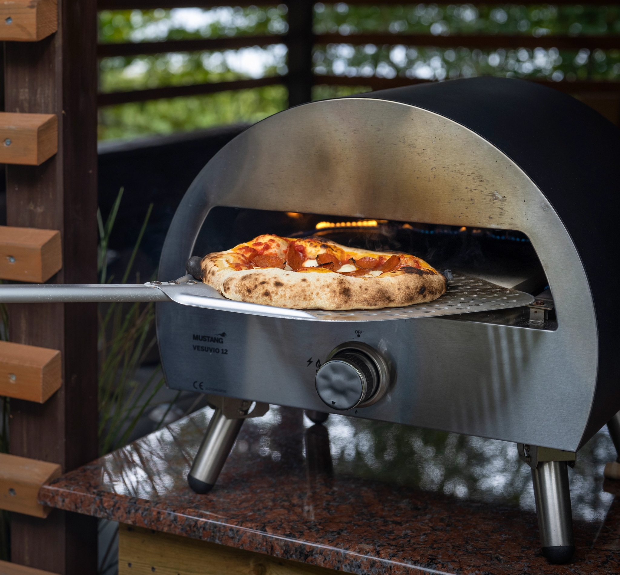 En svart kolgrill från Broil King står på en träaltan med gröna träd i bakgrunden