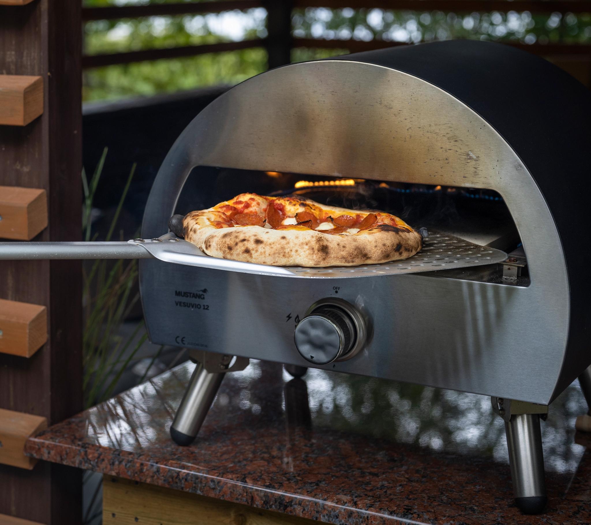 En svart kolgrill från Broil King står på en träaltan med gröna träd i bakgrunden