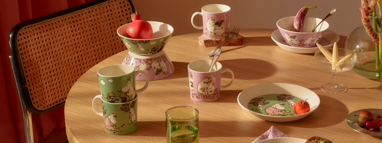 Puinen pöytä on katettu vaaleanpunaisilla ja vihreillä Muumi-aiheisilla astioilla