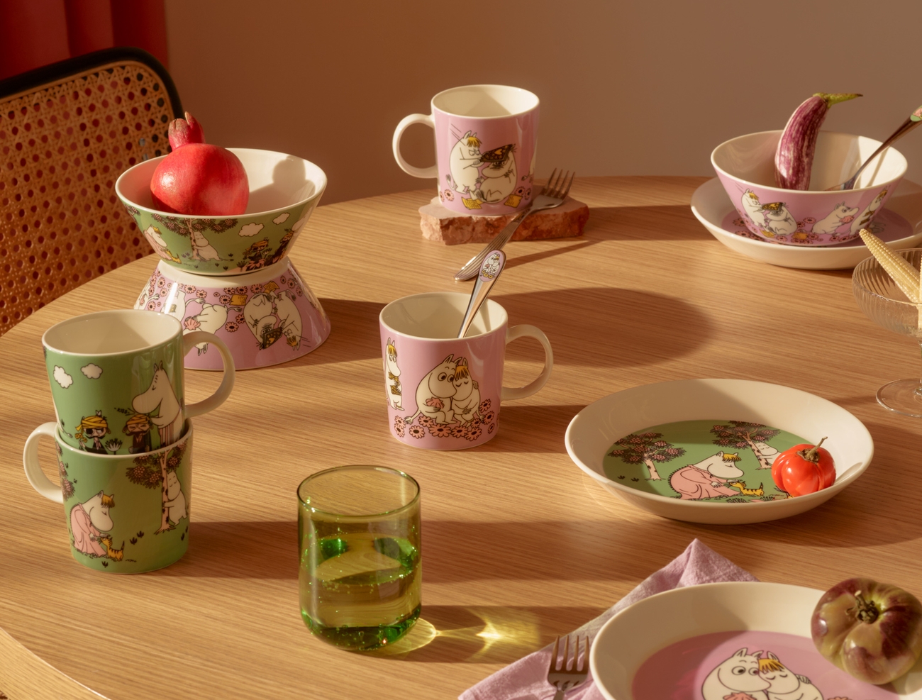 Puinen pöytä on katettu vaaleanpunaisilla ja vihreillä Muumi-aiheisilla astioilla