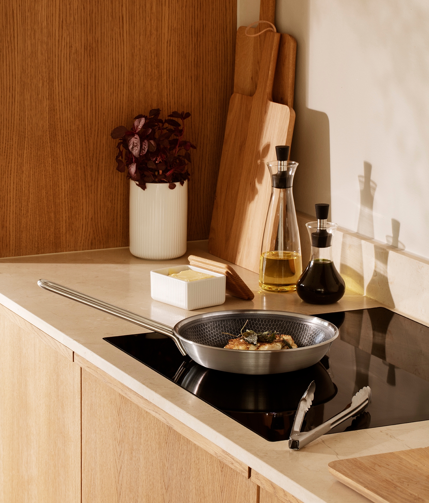 Närbild på en induktionshäll där en silvrig stekpanna steker mat