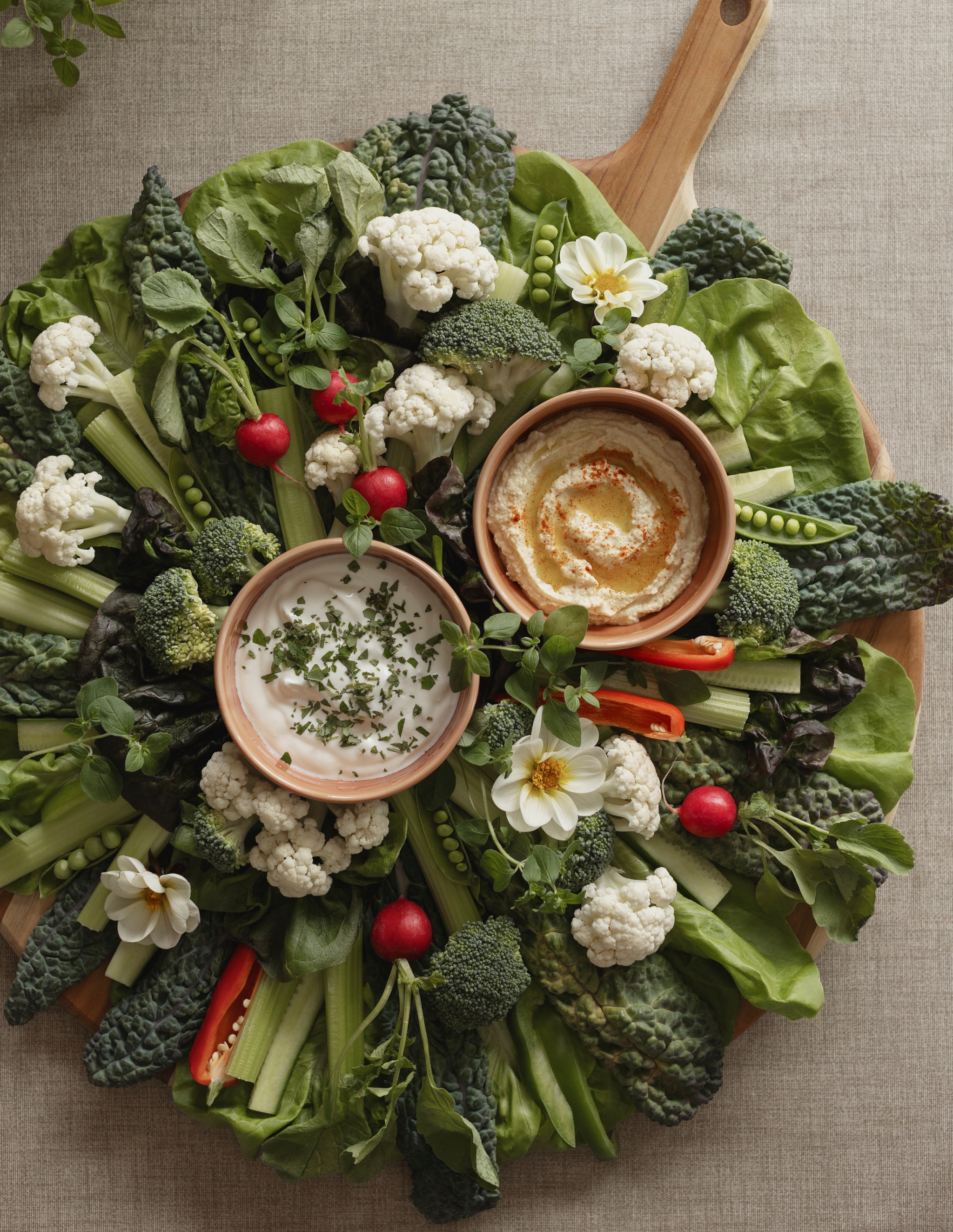 Färgglad grönsaksbricka med blomkål, broccoli, rädisor och selleri runt två skålar med dippsåser.