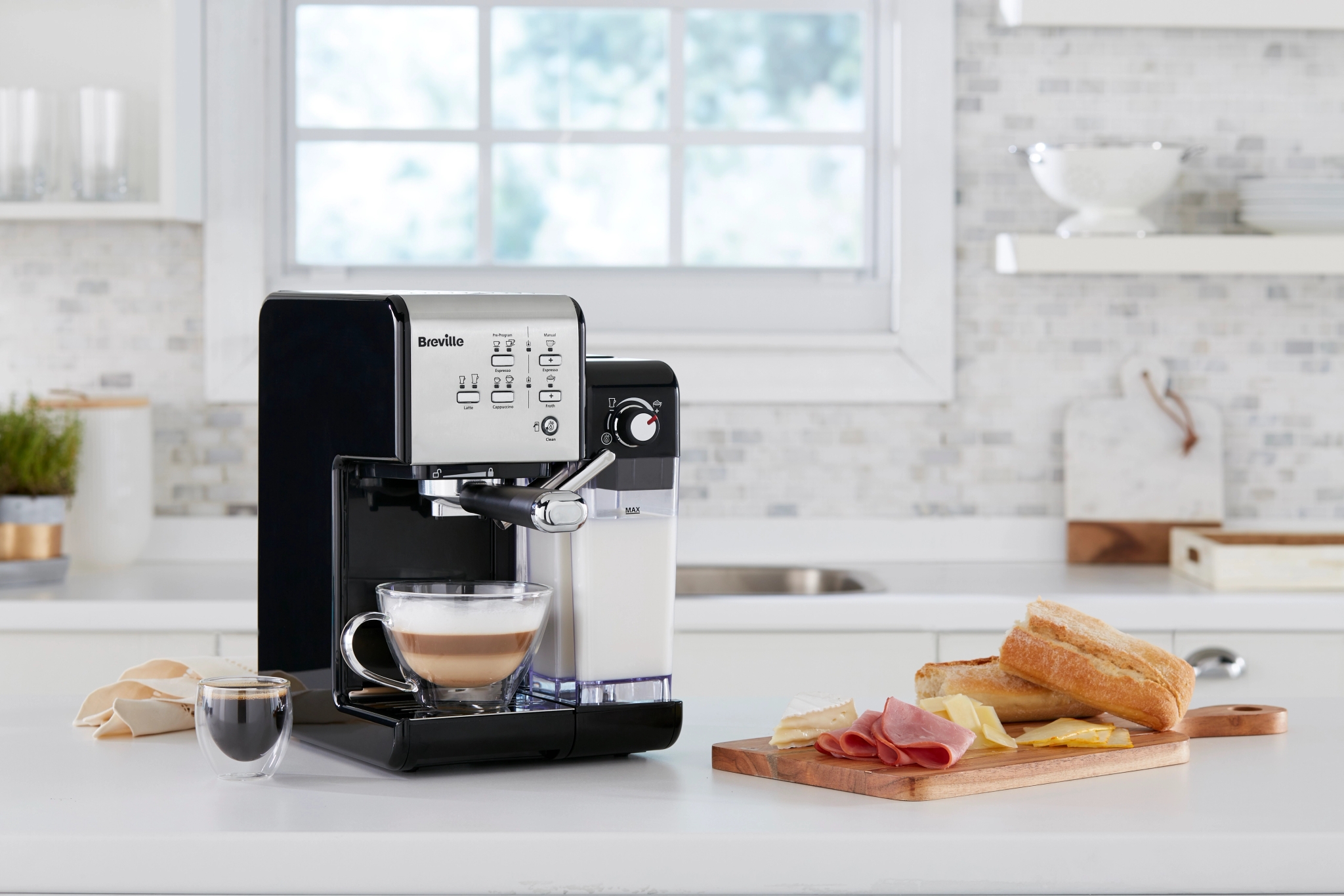Breville-espressokone valmistaa lattea keittiötasolla, vierellään espressoannos ja tarjotin, jossa on naposteltavaa.