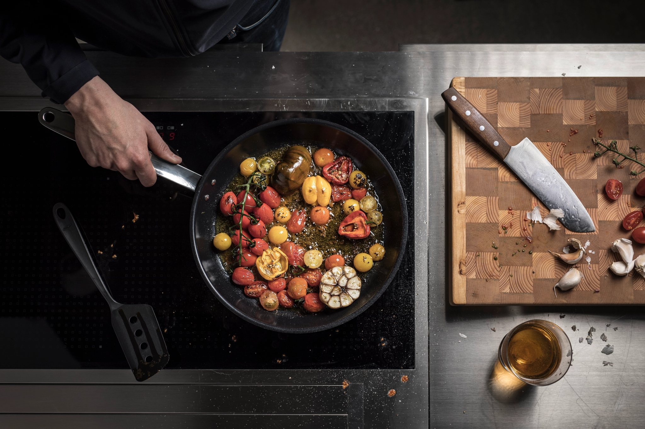 Fiskars paistinpannu liedellä täynnä tomatteja ja valkosipulia 