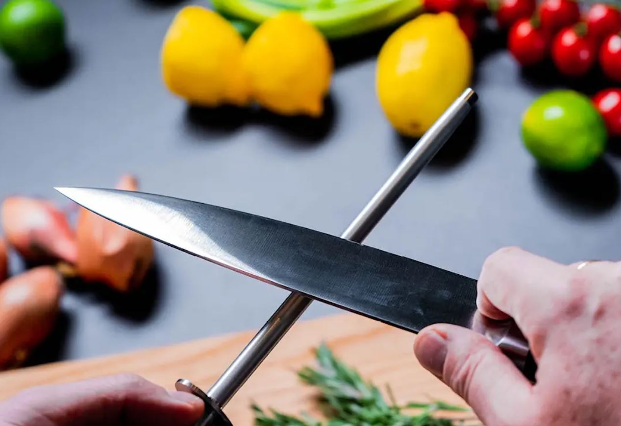 en person som vässar en kniv i köket med sitt skärpstål