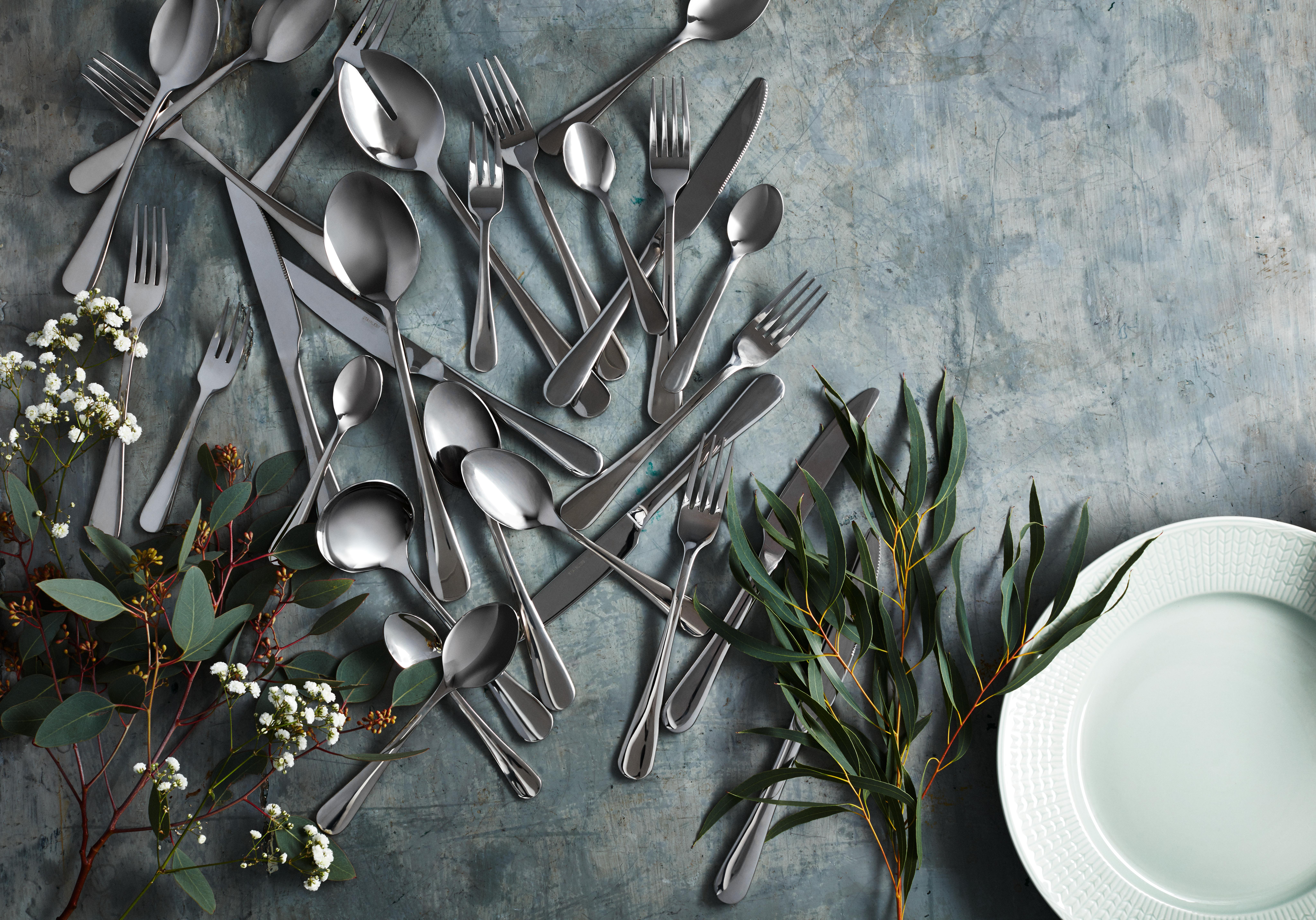 Lusikat haarukat ja veitset sekaisin pöydällä kukkien ja lautasen kera