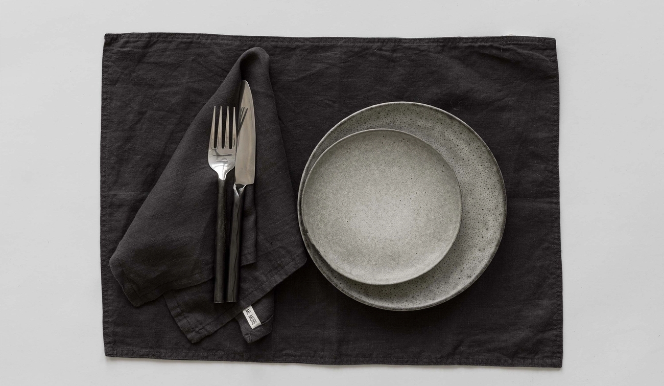 Svart bordstablett i linne med tallrikar och bestick på