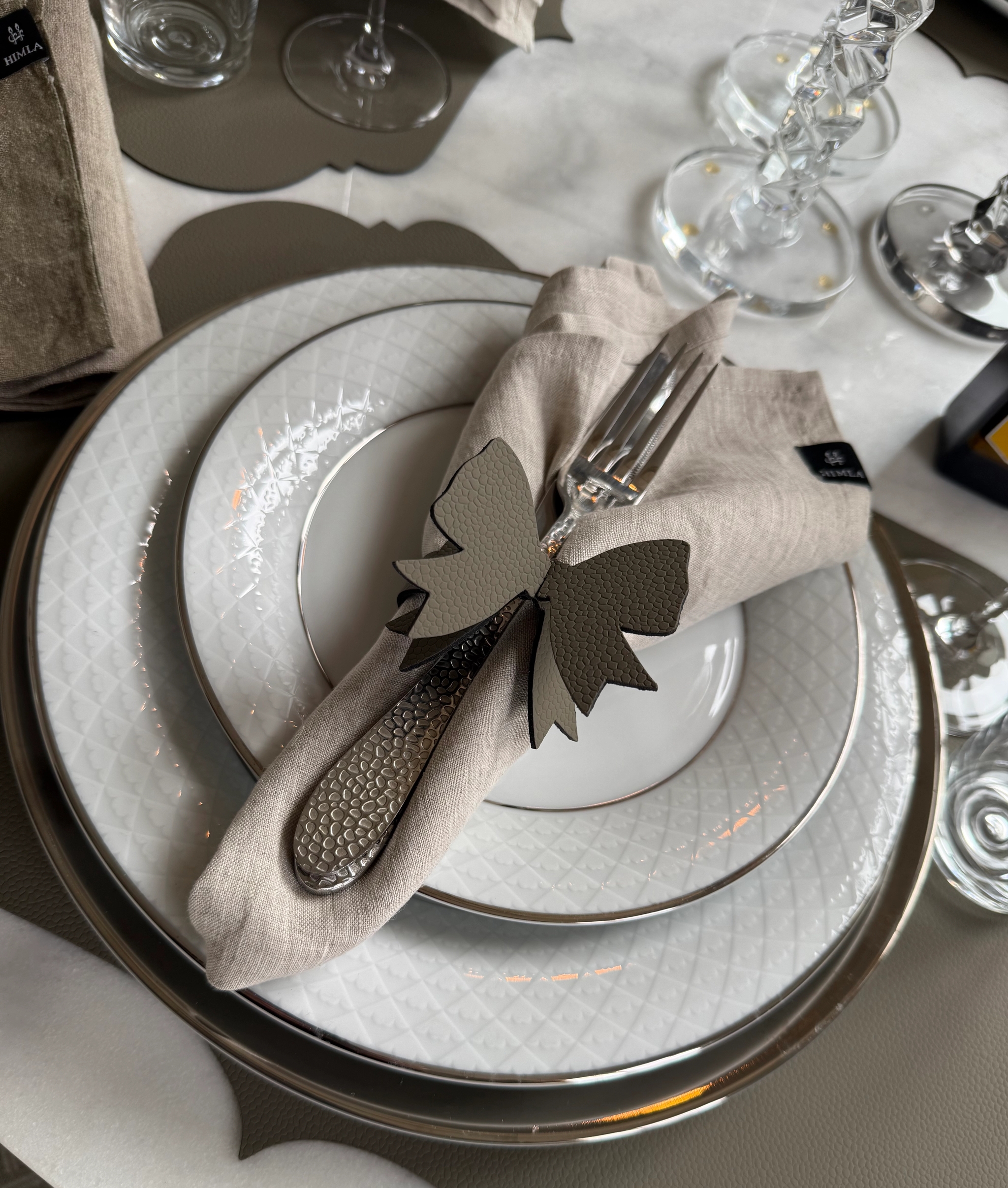 Elegant dukning med vita tallrikar, linneservett, silverbestick och dekorativ rosett.