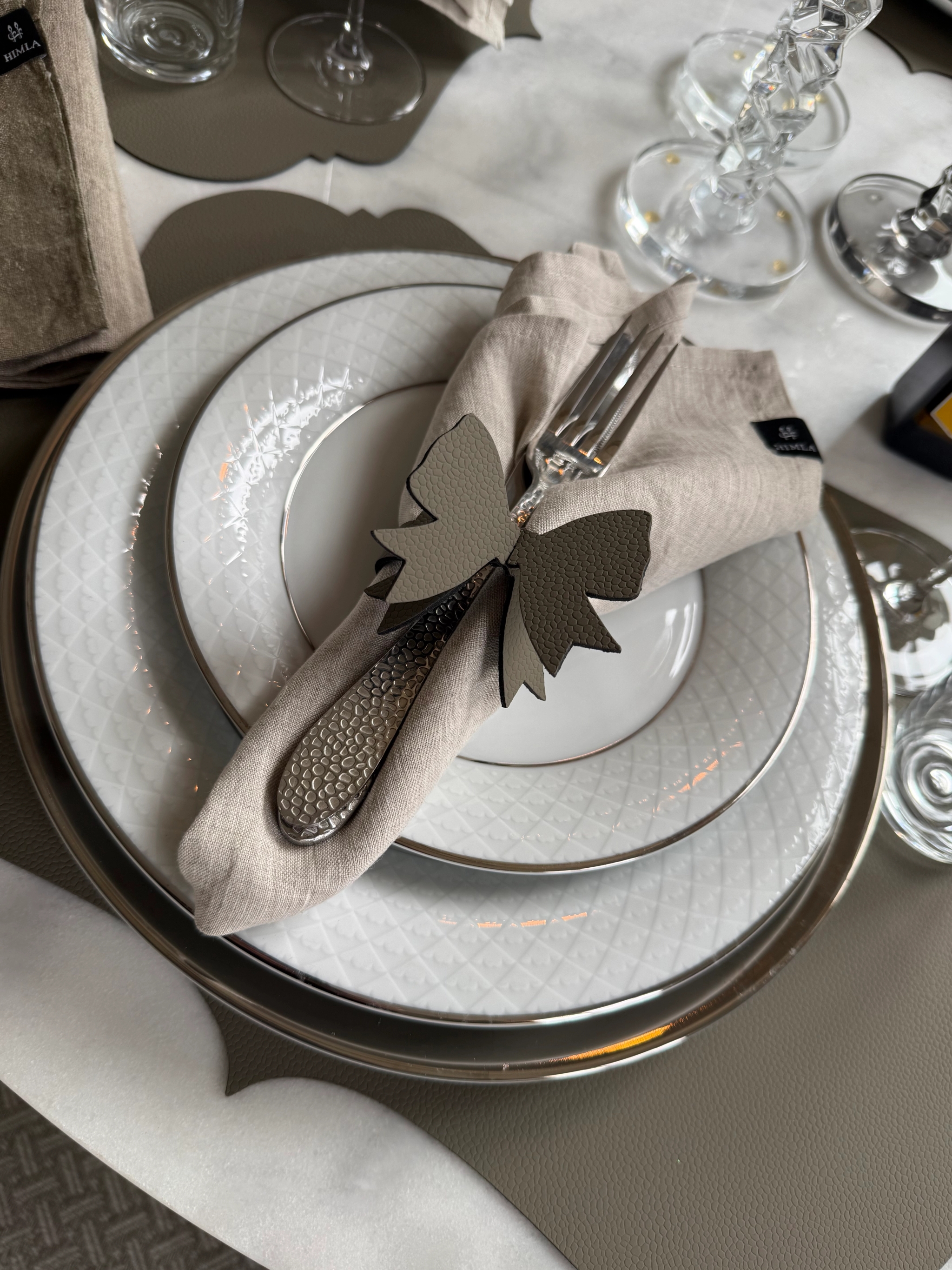 Elegant dukning med vita tallrikar, linneservett, silverbestick och dekorativ rosett.