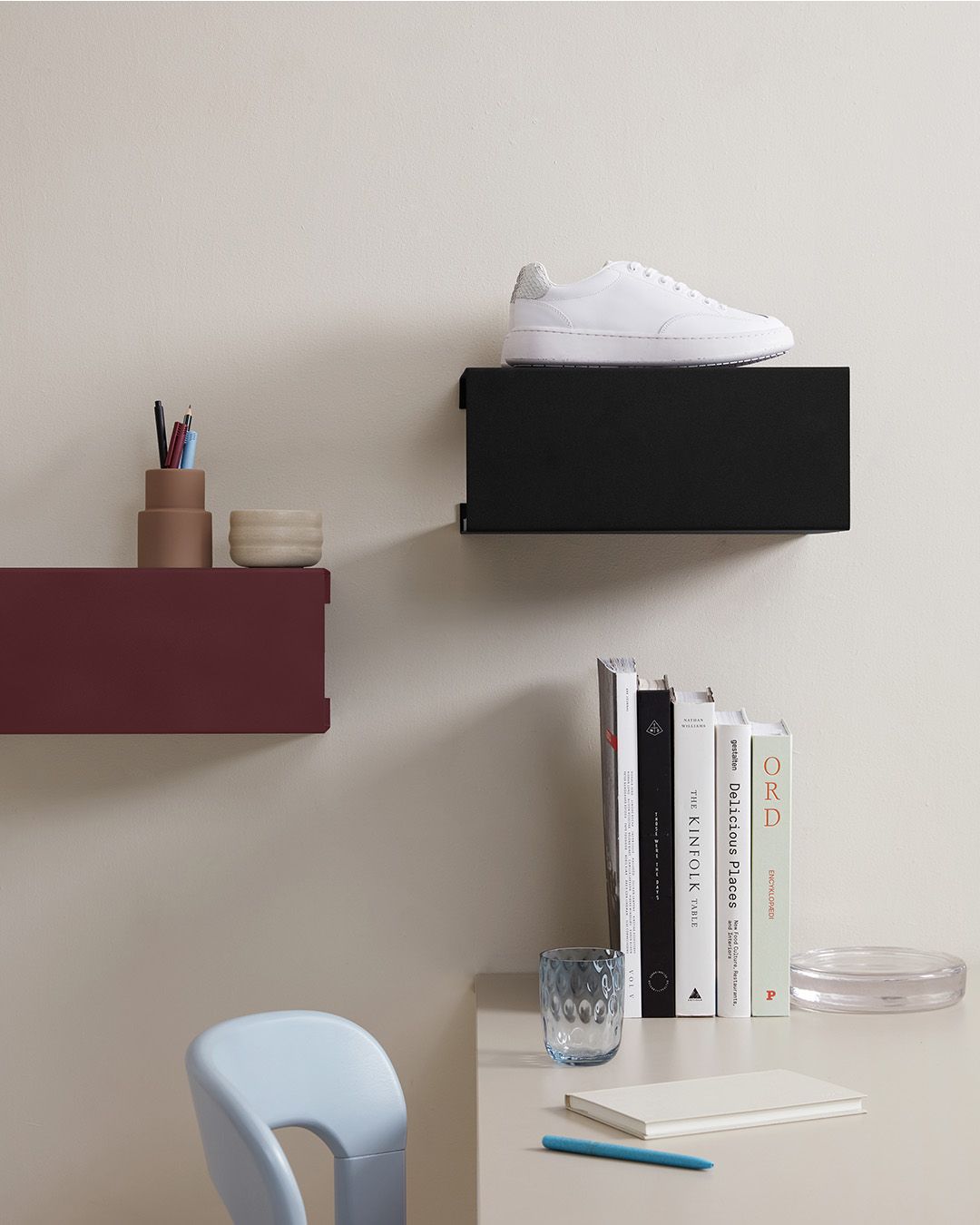 Stilren arbetsplats med vägghyllor, böcker, skrivbord och en vit sneaker mot en beige vägg.