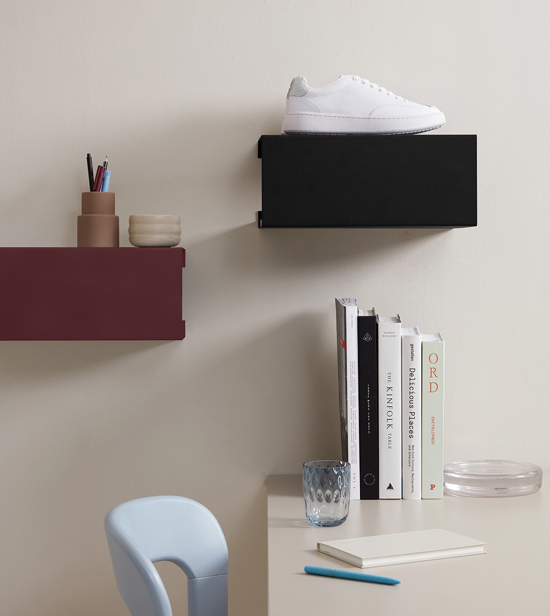 Stilren arbetsplats med vägghyllor, böcker, skrivbord och en vit sneaker mot en beige vägg.