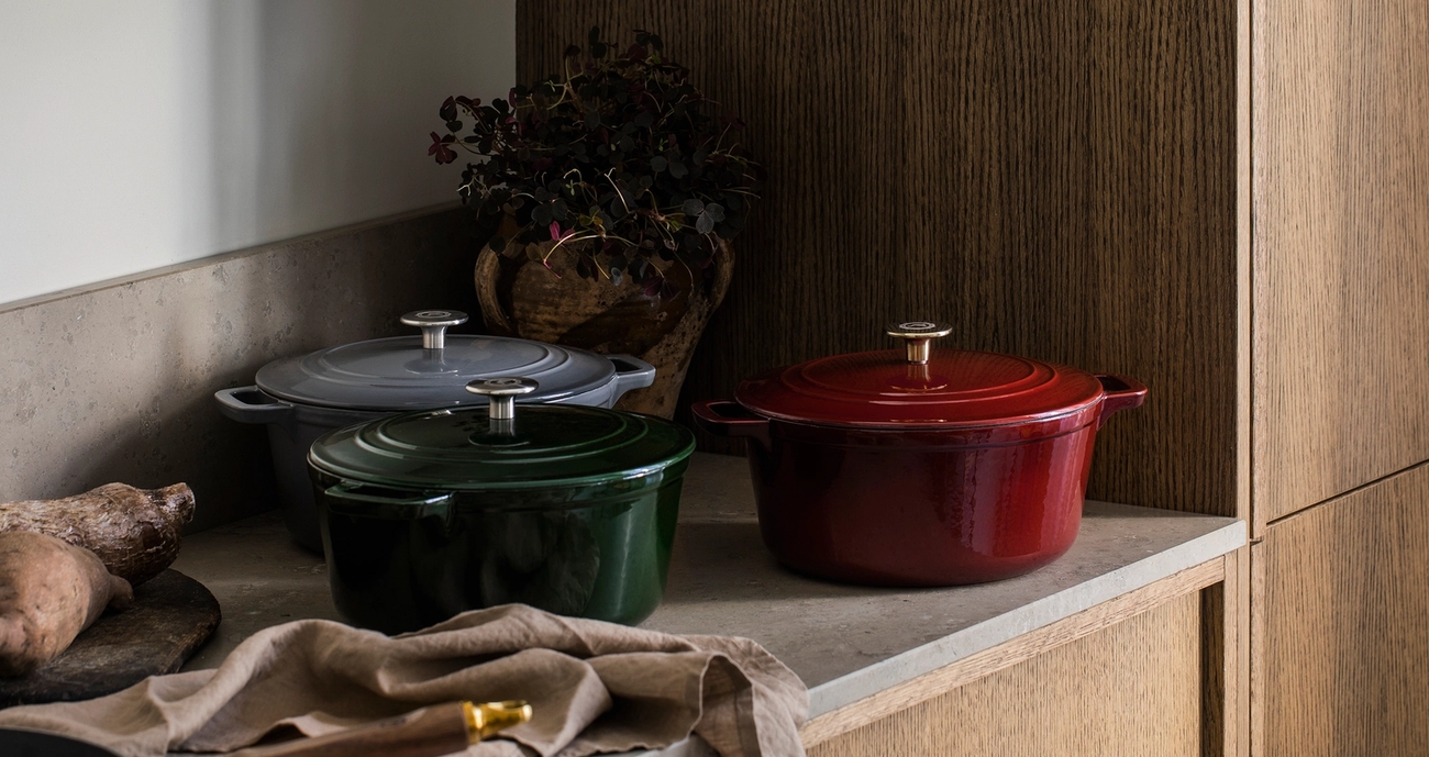 Punaisia, vihreitä ja harmaita valurautaisia kattiloita keittiön tiskillä.