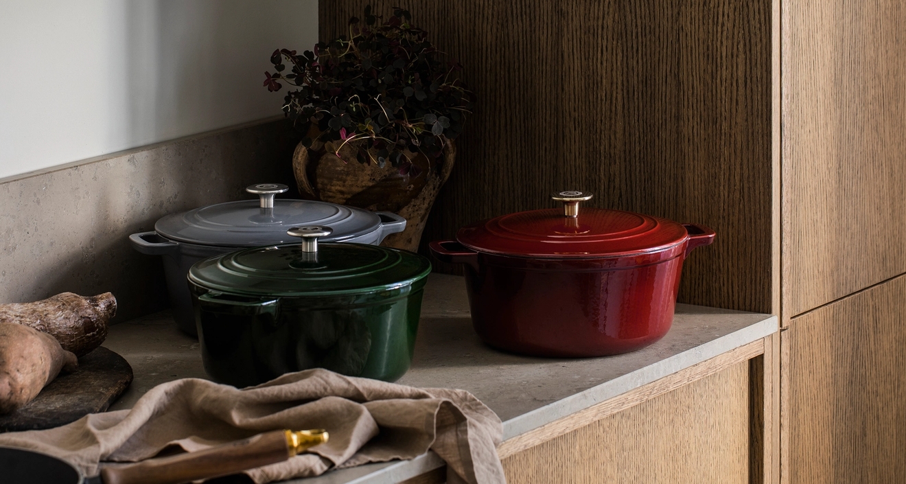 Punaisia, vihreitä ja harmaita valurautaisia kattiloita keittiön tiskillä.