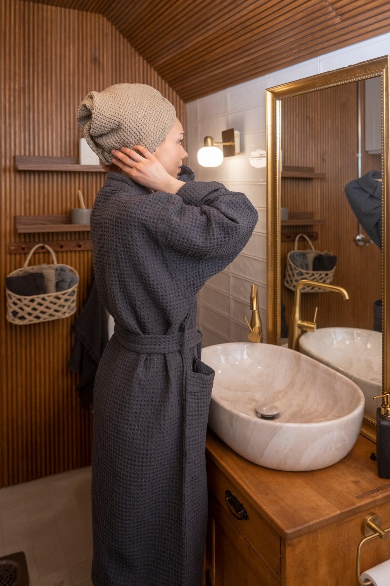 En dame i morgenkåpe surrer håret i et håndkle på et bad