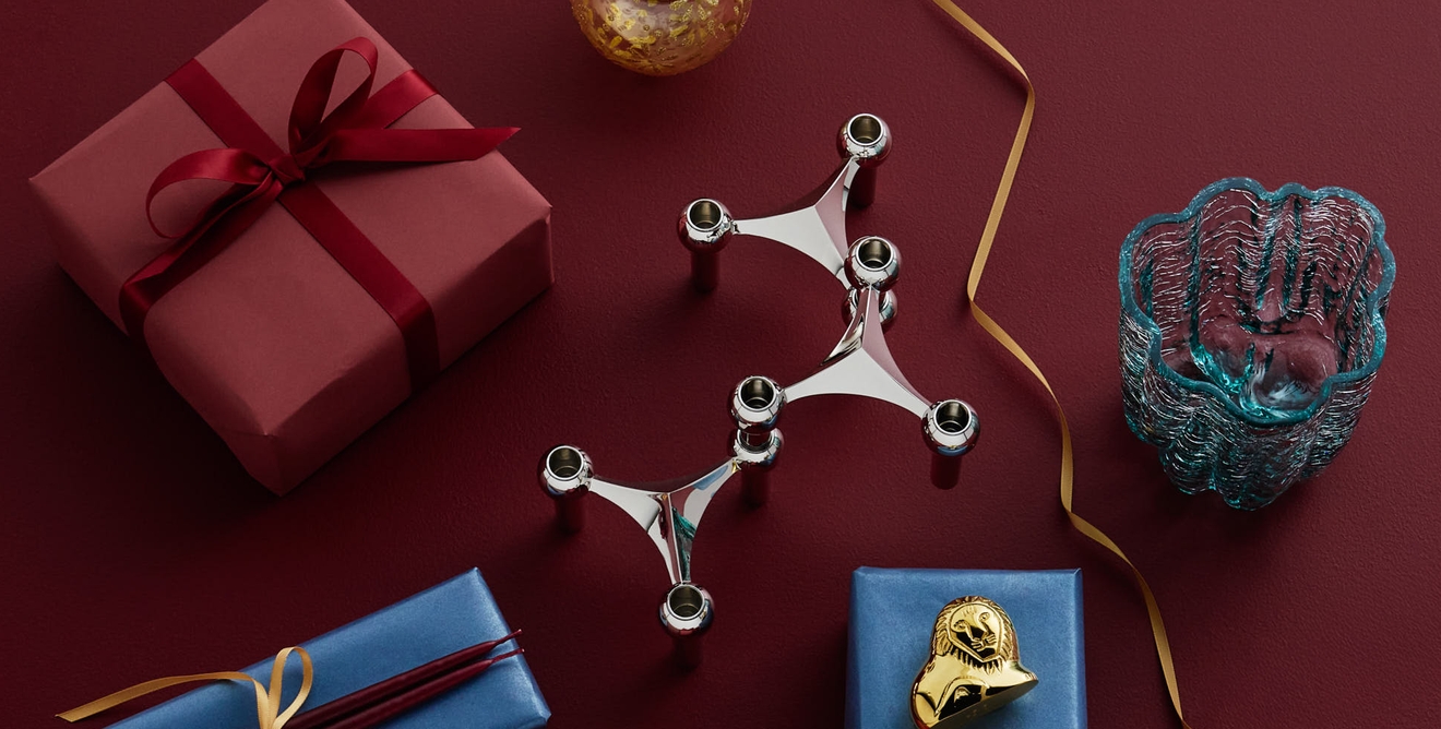 Festligt arrangemang av presenter, en silverljusstake, en guldprydnad och dekorativa föremål på en djupröd yta.