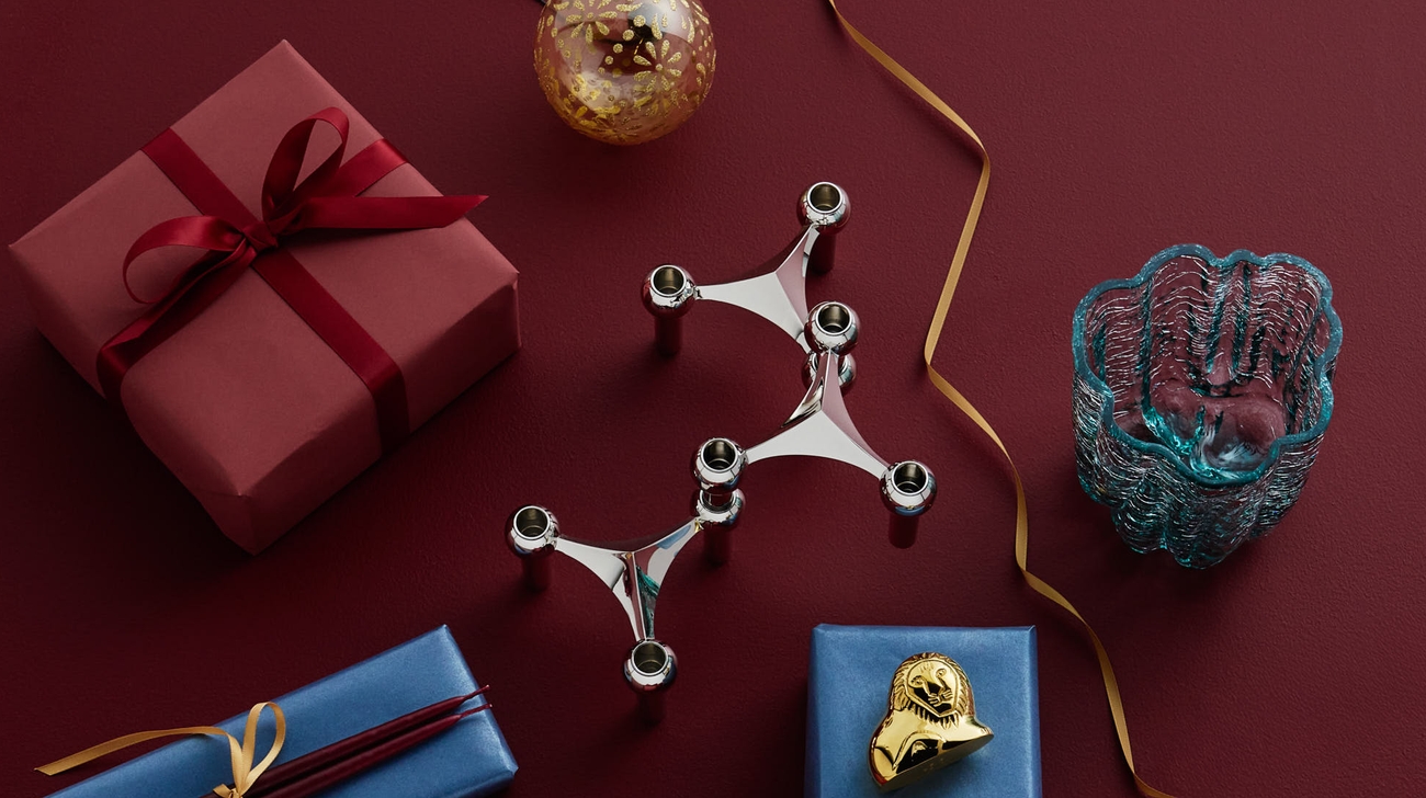 Festligt arrangemang av presenter, en silverljusstake, en guldprydnad och dekorativa föremål på en djupröd yta.