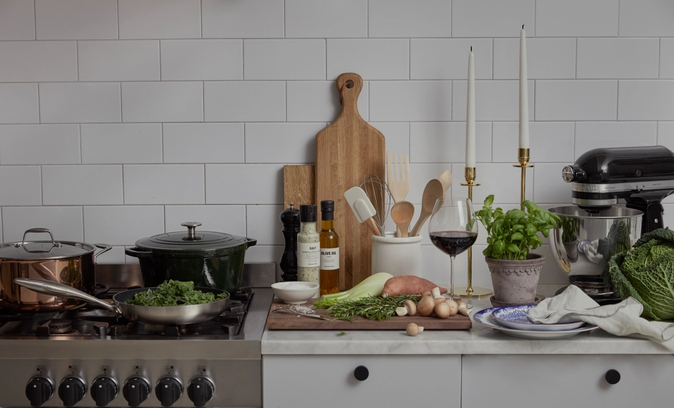 Keittiötaso ja liesi, jotka on katettu tuoreilla raaka-aineilla, ruoanlaittovälineillä ja yleiskoneella