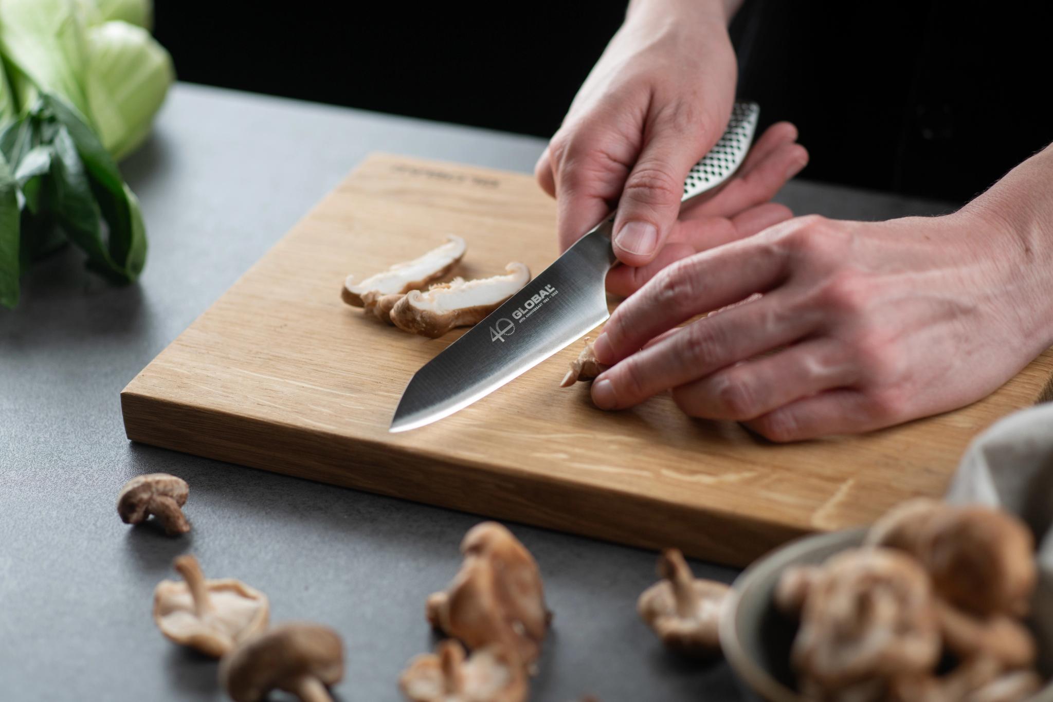 Hands using a knife to slice mushrooms on a wooden cutting board.